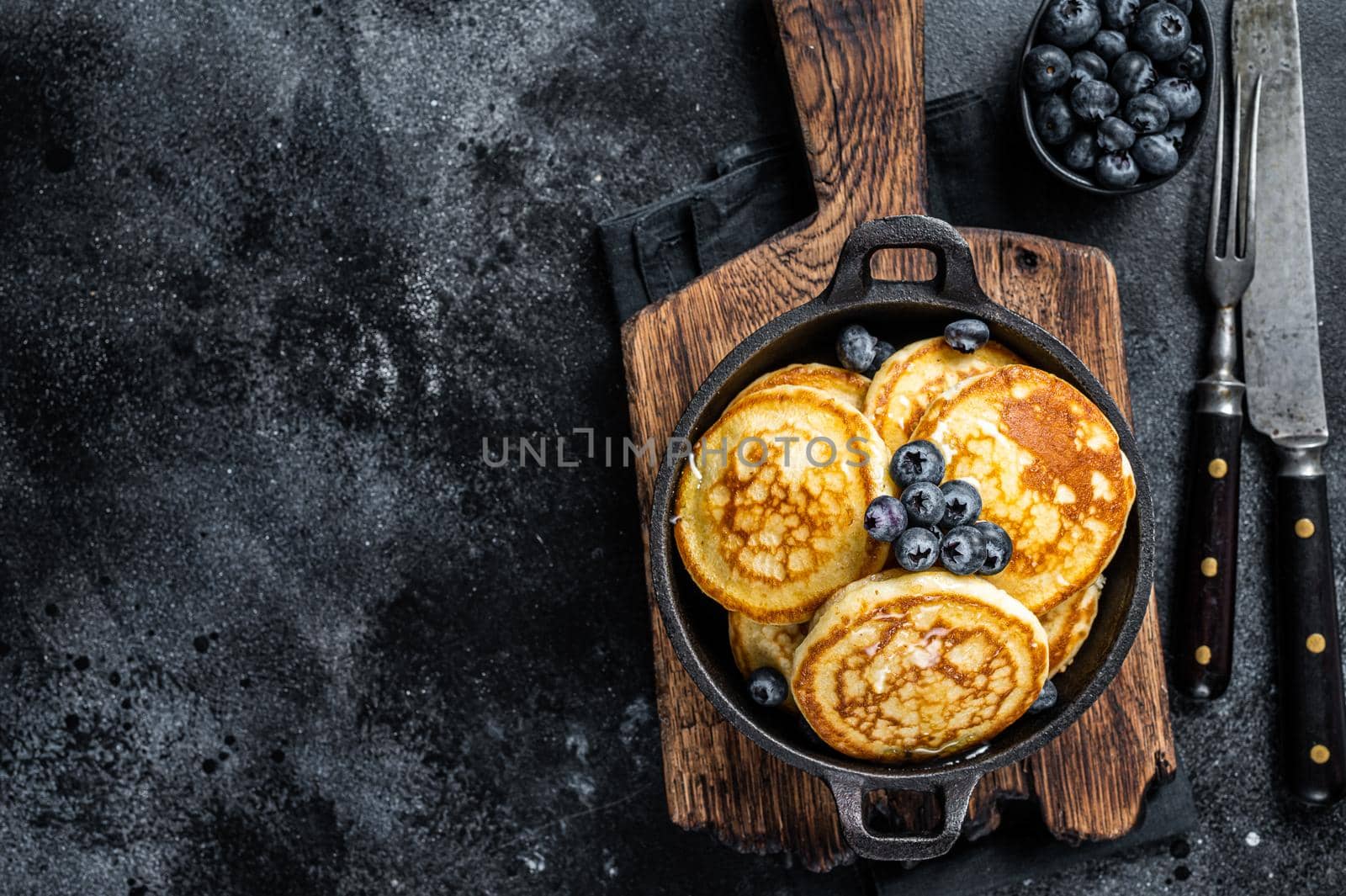 Pancakes with fresh blueberries and maple syrup in a pan. Black background. Top View. Copy space by Composter