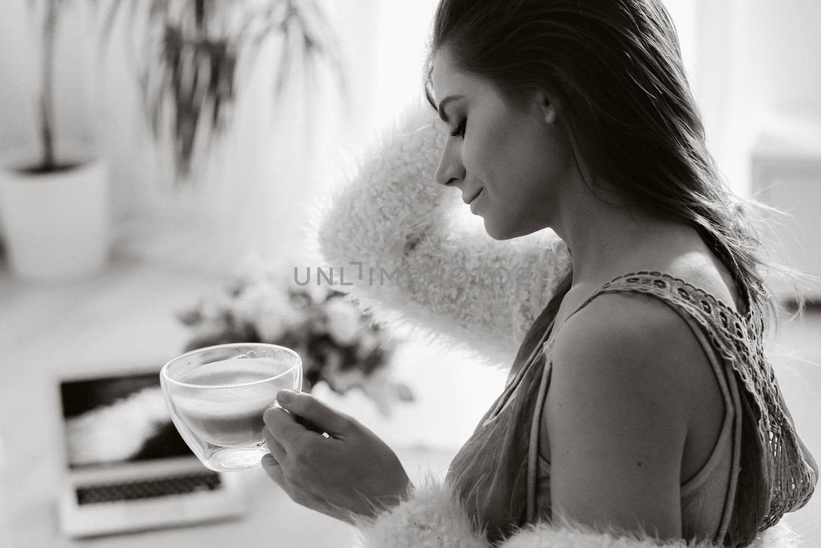 a relaxed girl at home drinks coffee and watches a movie.Domestic calm.The girl is sitting comfortably on the sofa and drinking coffee.black and white photo.
