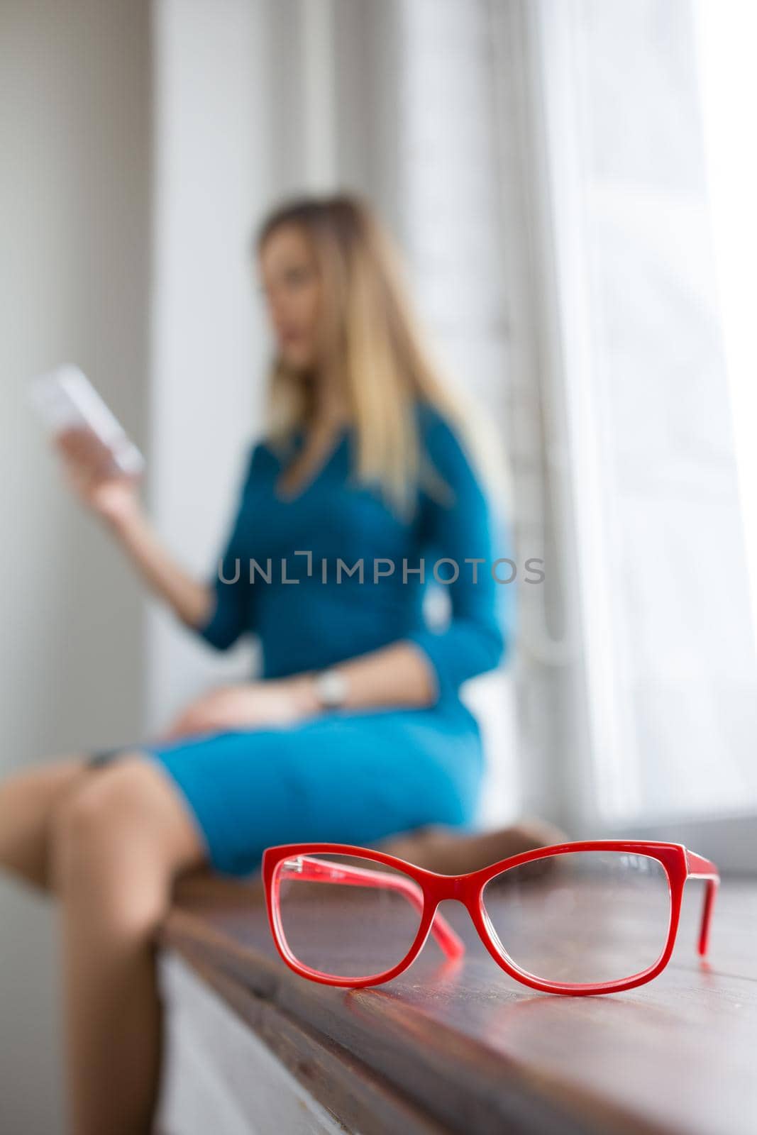 Attractive blonde business woman holds smartphone near window, de-focused, telephoto
