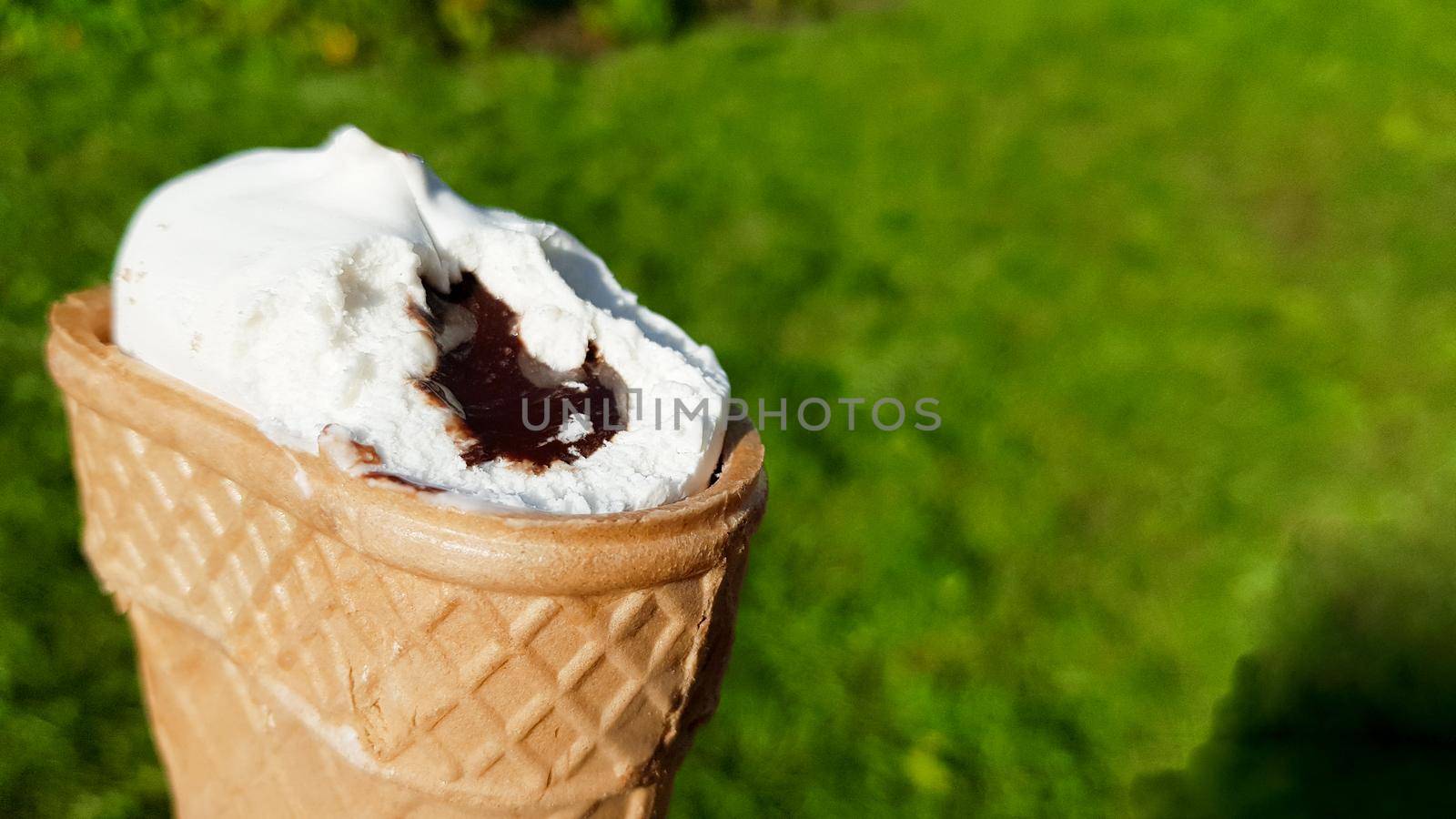 bitten ice cream in a waffle cup with chocolate filling. Bitten white ice cream with caramel on a background of green grass in summer.