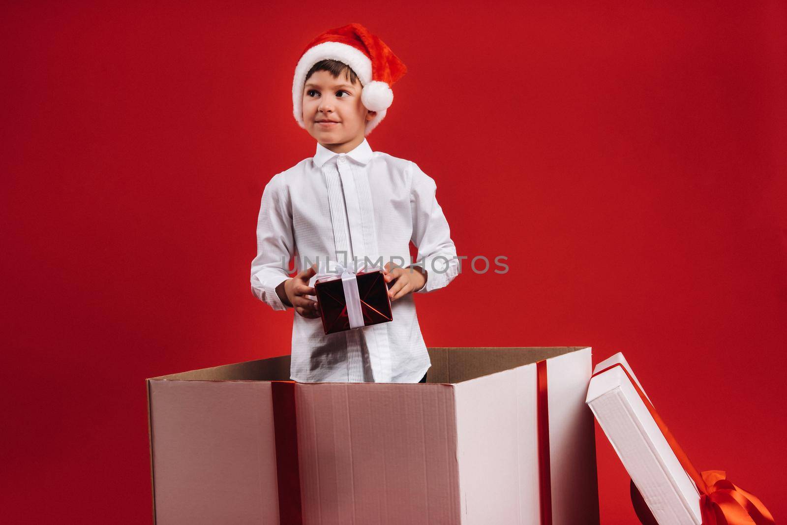 A little boy stands in a gift box with a Christmas present in his hands.