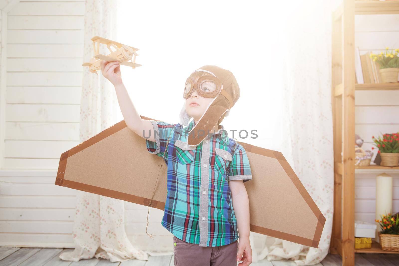 Children boy wearing pilot costume making ready to fly gesture standing on living room wooden floor at home. .