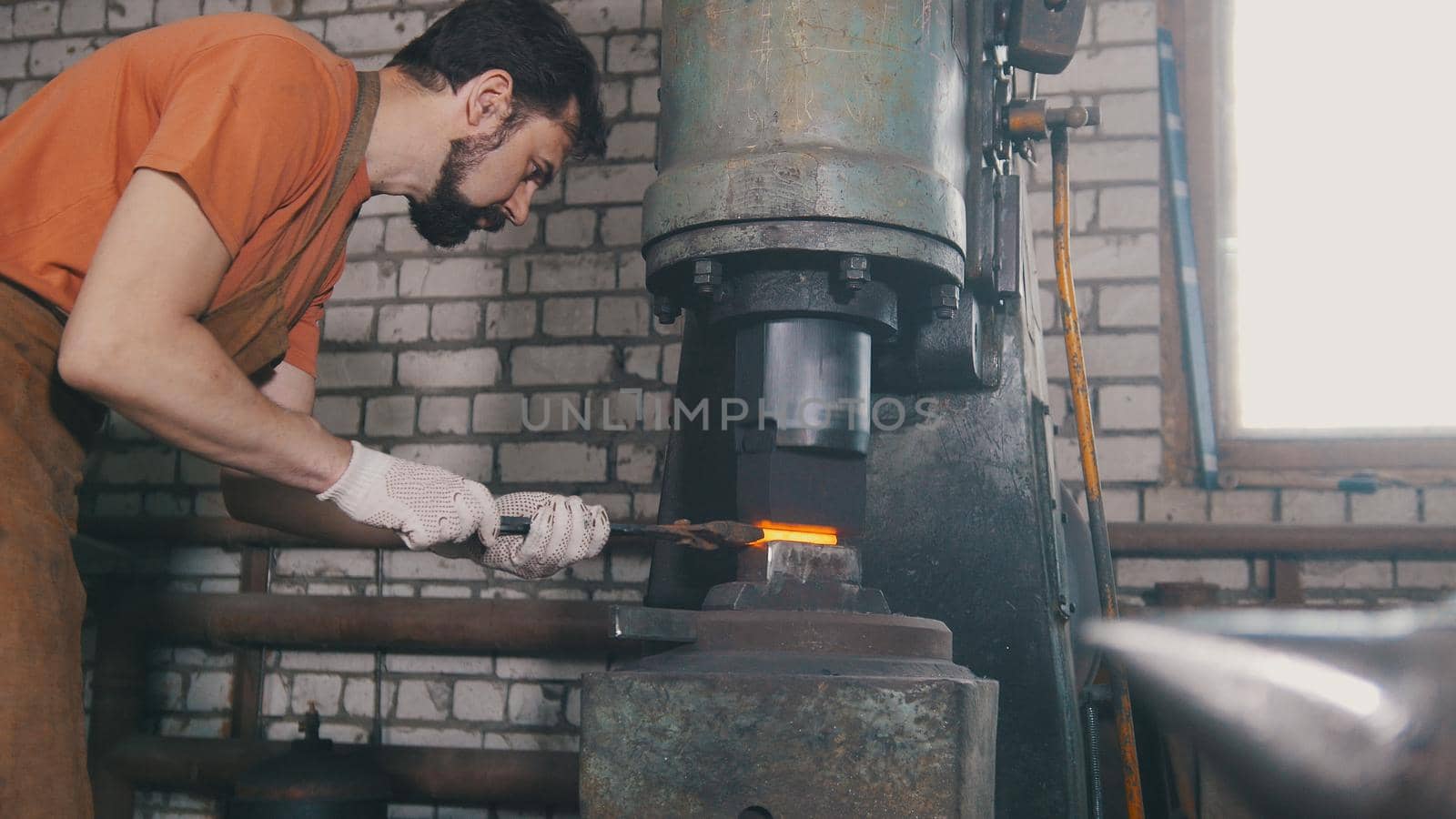 Man blacksmith forges the metal at the mechanical hammer - small business, close up