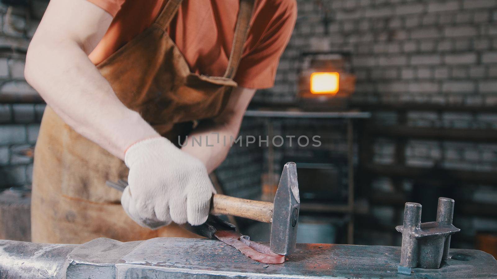 The blacksmith with a beard gives shape with the help of a hammer on the anvil to a red-hot metal productproduct