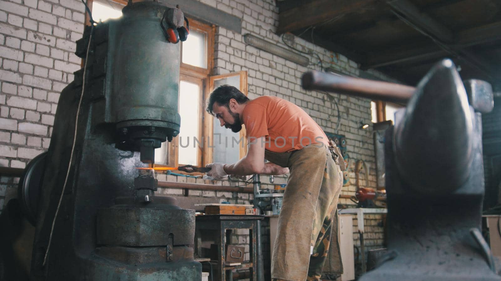 Man blacksmith forges the metal at the mechanical hammer - small business,