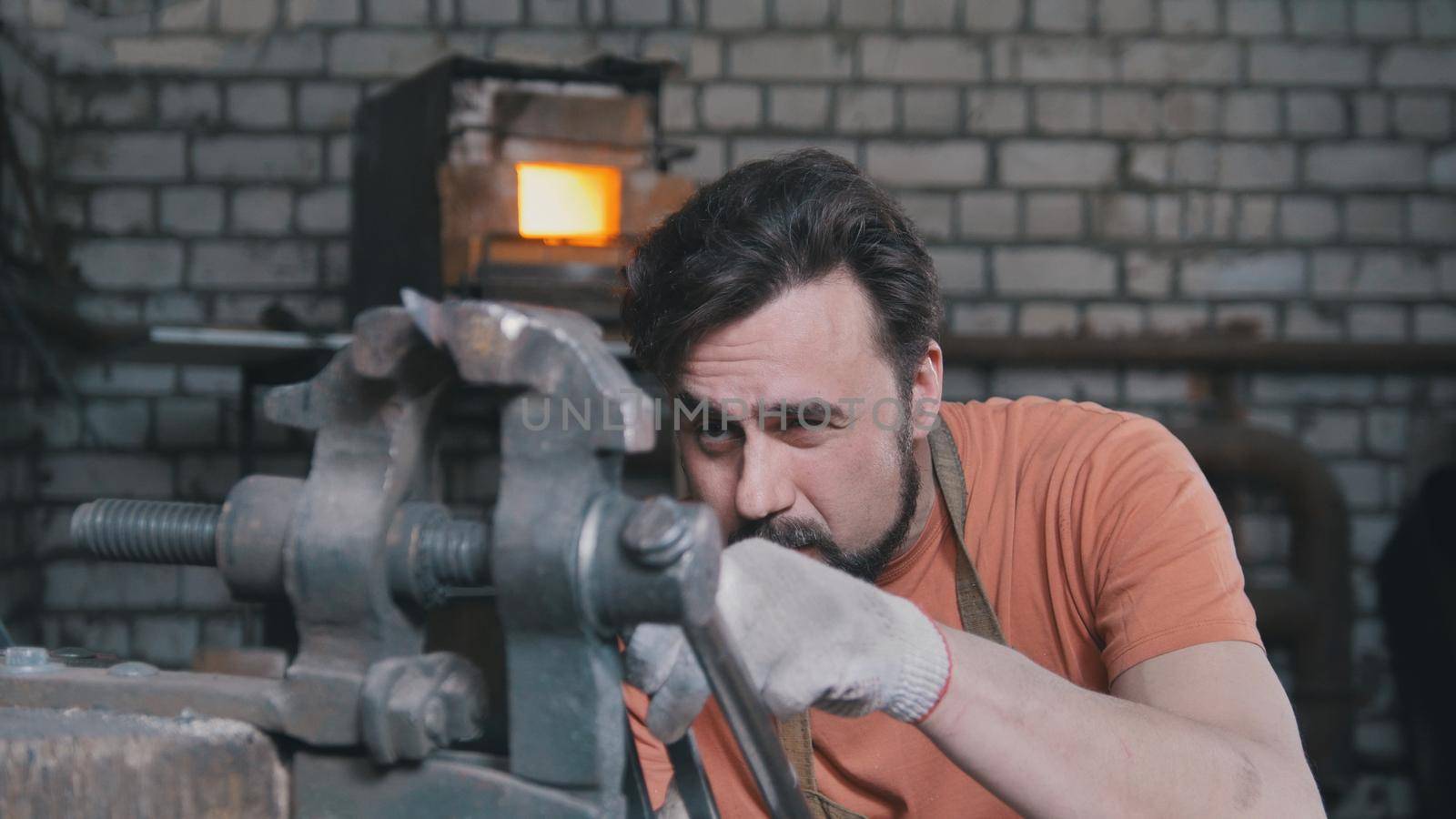 Blacksmith bends metal knife with gripe in workshop forge, portrait, telephoto