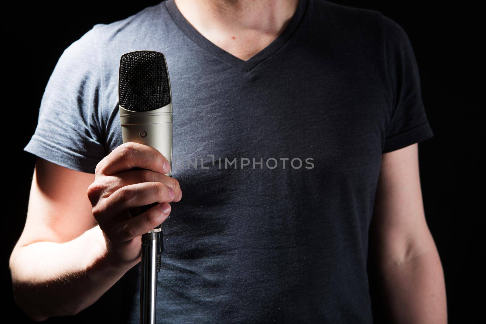 Male singer on the stage holding a microphone on a dark background