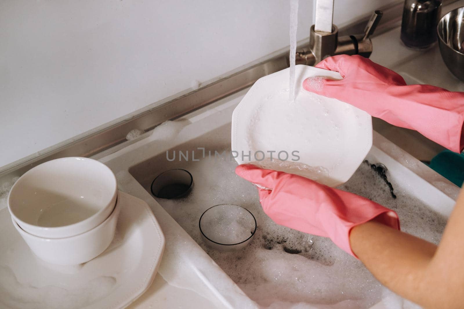 housewife girl in pink gloves washes dishes by hand in the sink with detergent. The girl cleans the house and washes dishes in gloves at home