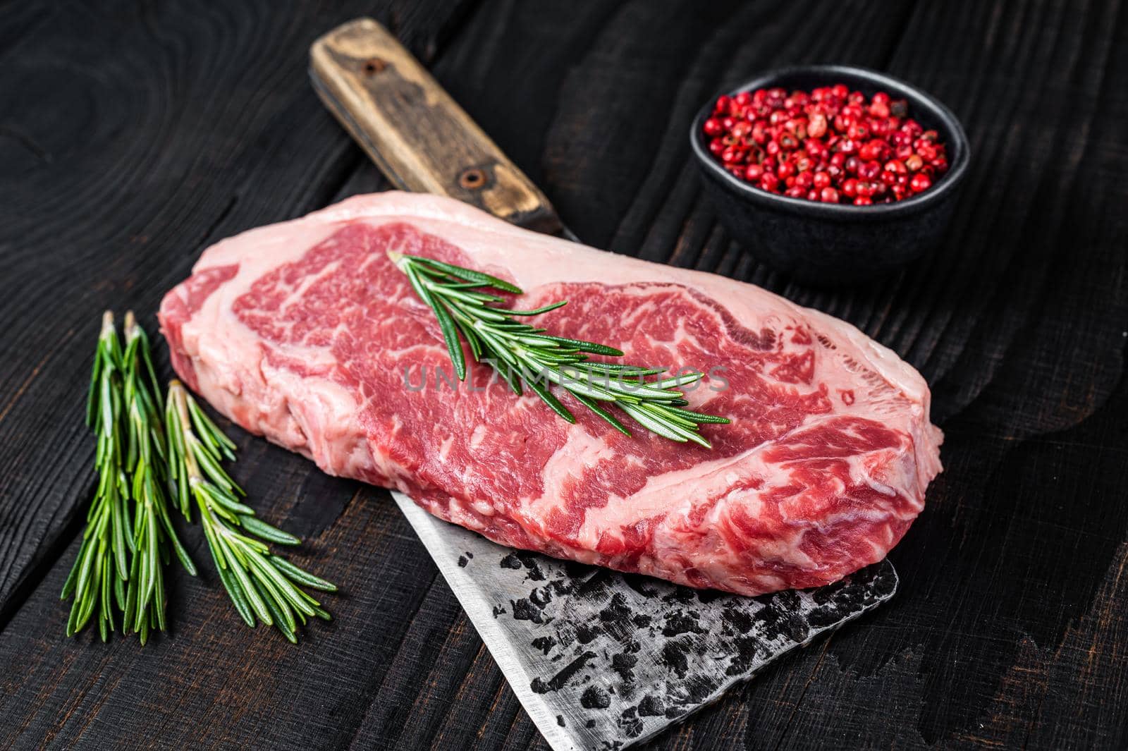 Fresh Raw new york strip beef steak on a butcher meat cleaver. Black wooden background. Top view.