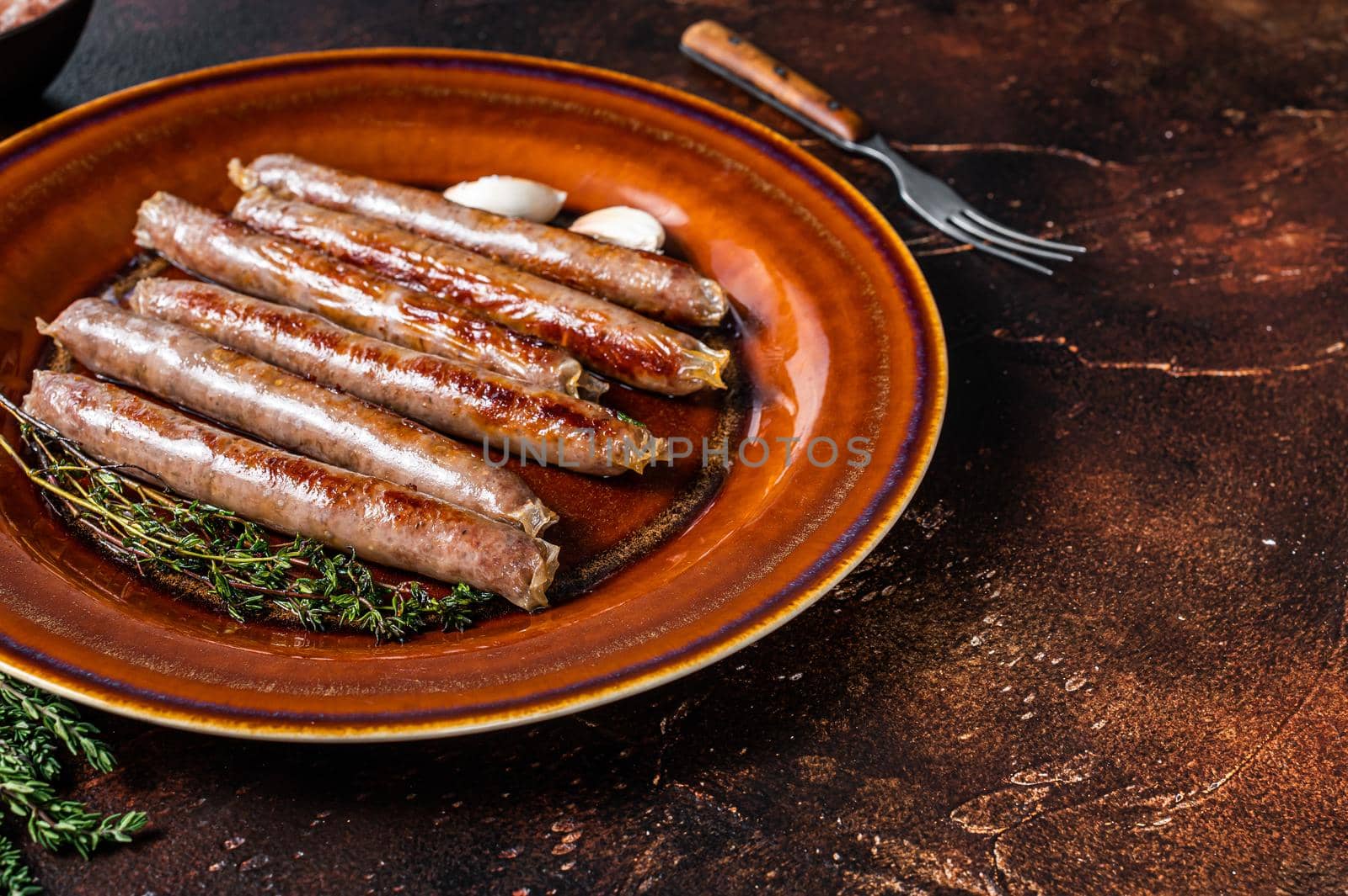 Grilled beef and pork meat sausage on rustic plate with thyme. Dark background. Top view. Copy space.