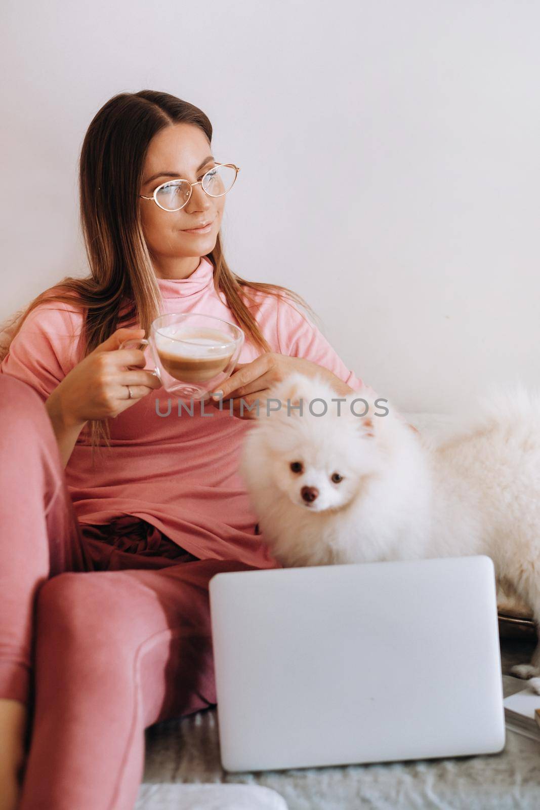 a girl in pajamas at home is working on a laptop with her dog Spitzer, the dog and its owner are resting on the couch and watching the laptop.Household chores by Lobachad