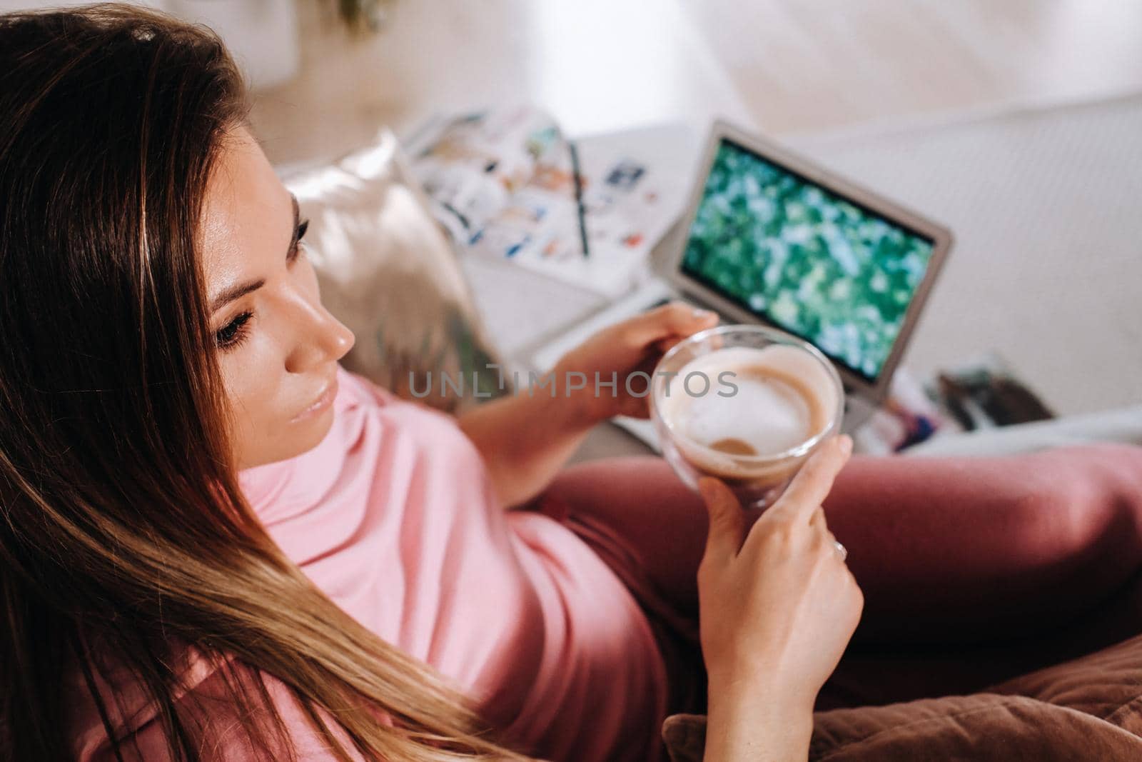a girl in the morning in pajamas at home working on a laptop with drinking coffee, a girl self-isolated at home and resting on the couch and watching a laptop.Household chores by Lobachad