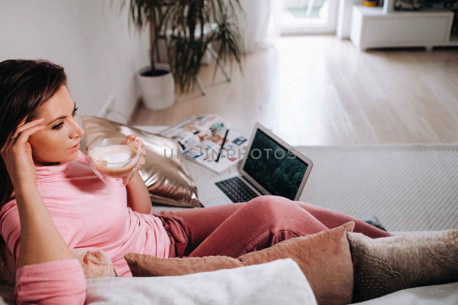 a girl in the morning in pajamas at home working on a laptop with drinking coffee, a girl self-isolated at home and resting on the couch and watching a laptop.Household chores.