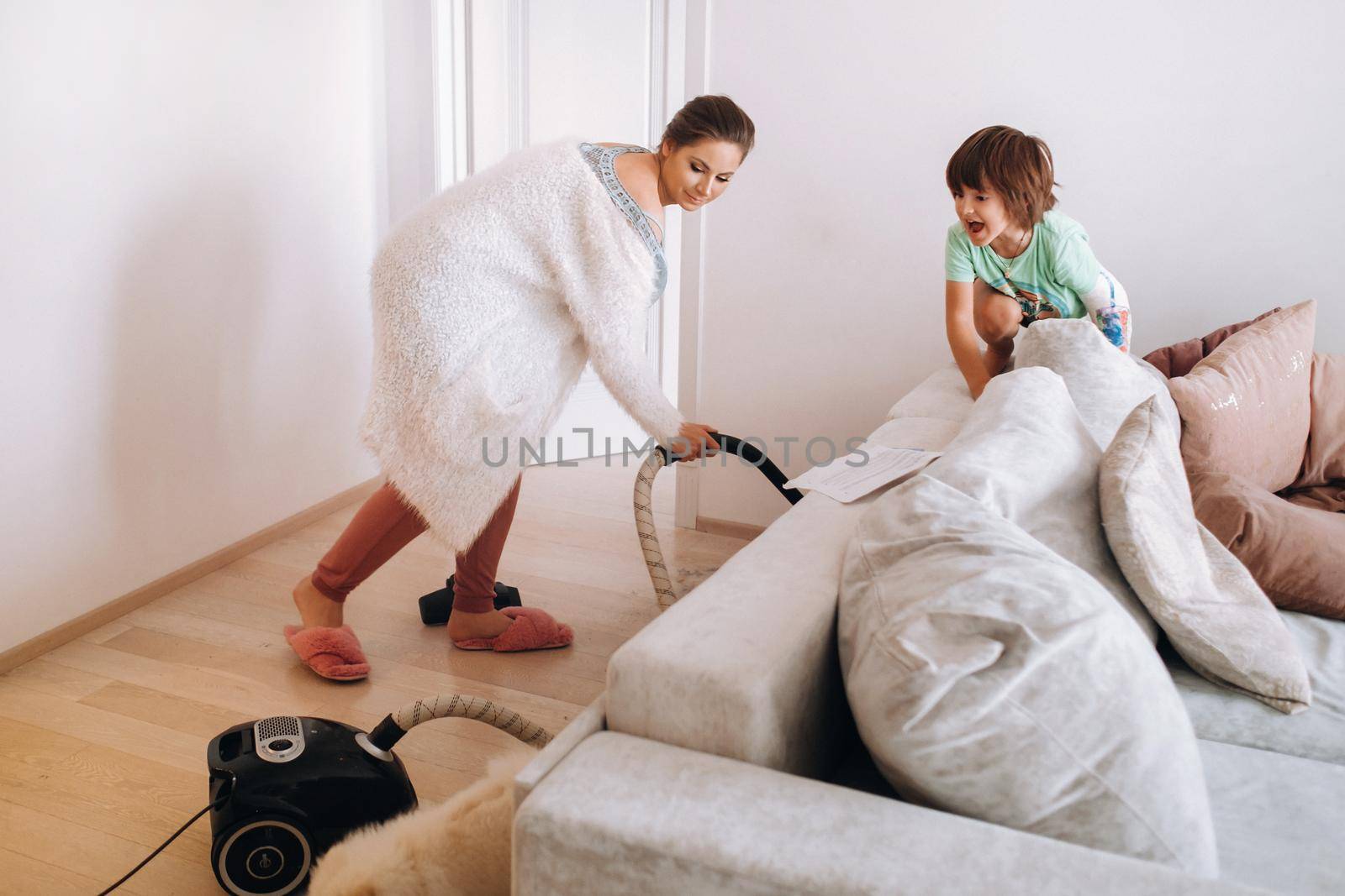 the mother vacuums the floor at home and the son watches and laughs at it.