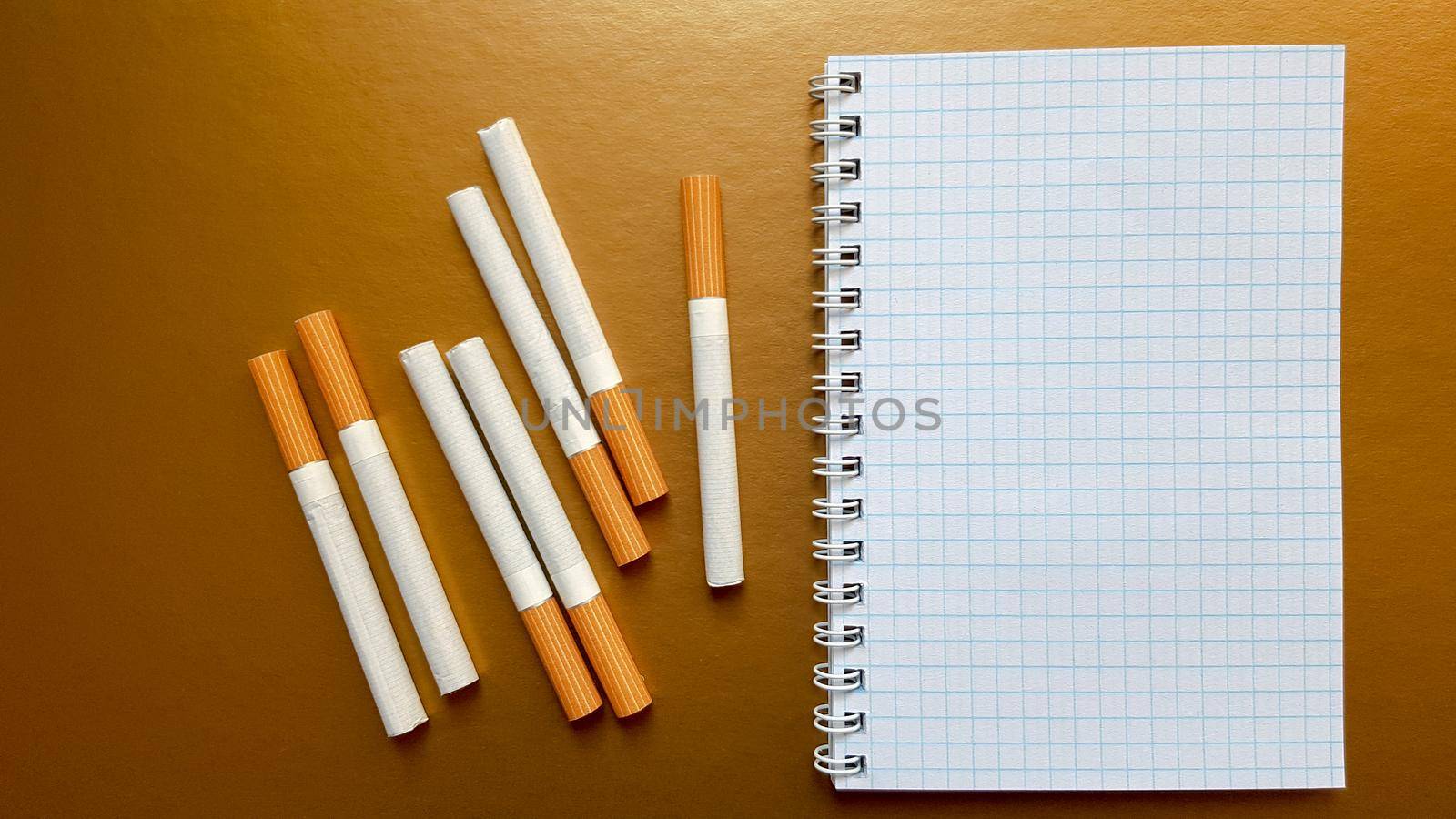 Notebook with cigarettes on top on a gold background.