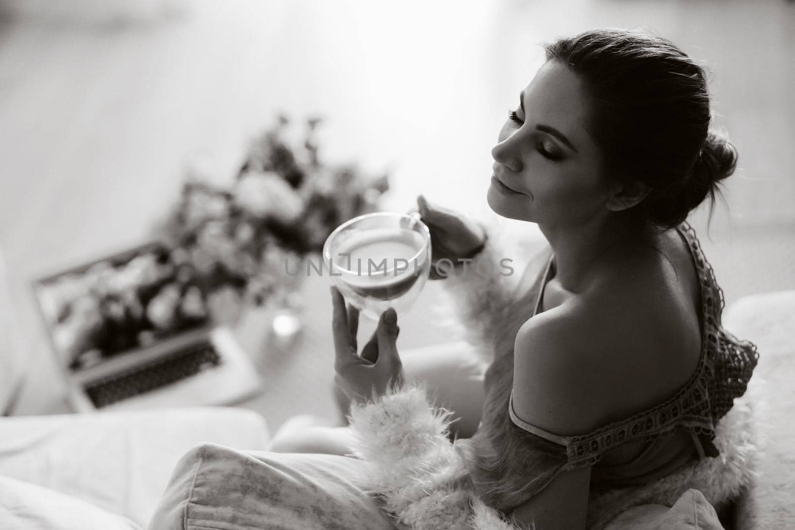 a relaxed girl at home drinks coffee and watches a movie.Domestic calm.The girl is sitting comfortably on the sofa and drinking coffee.black and white photo.