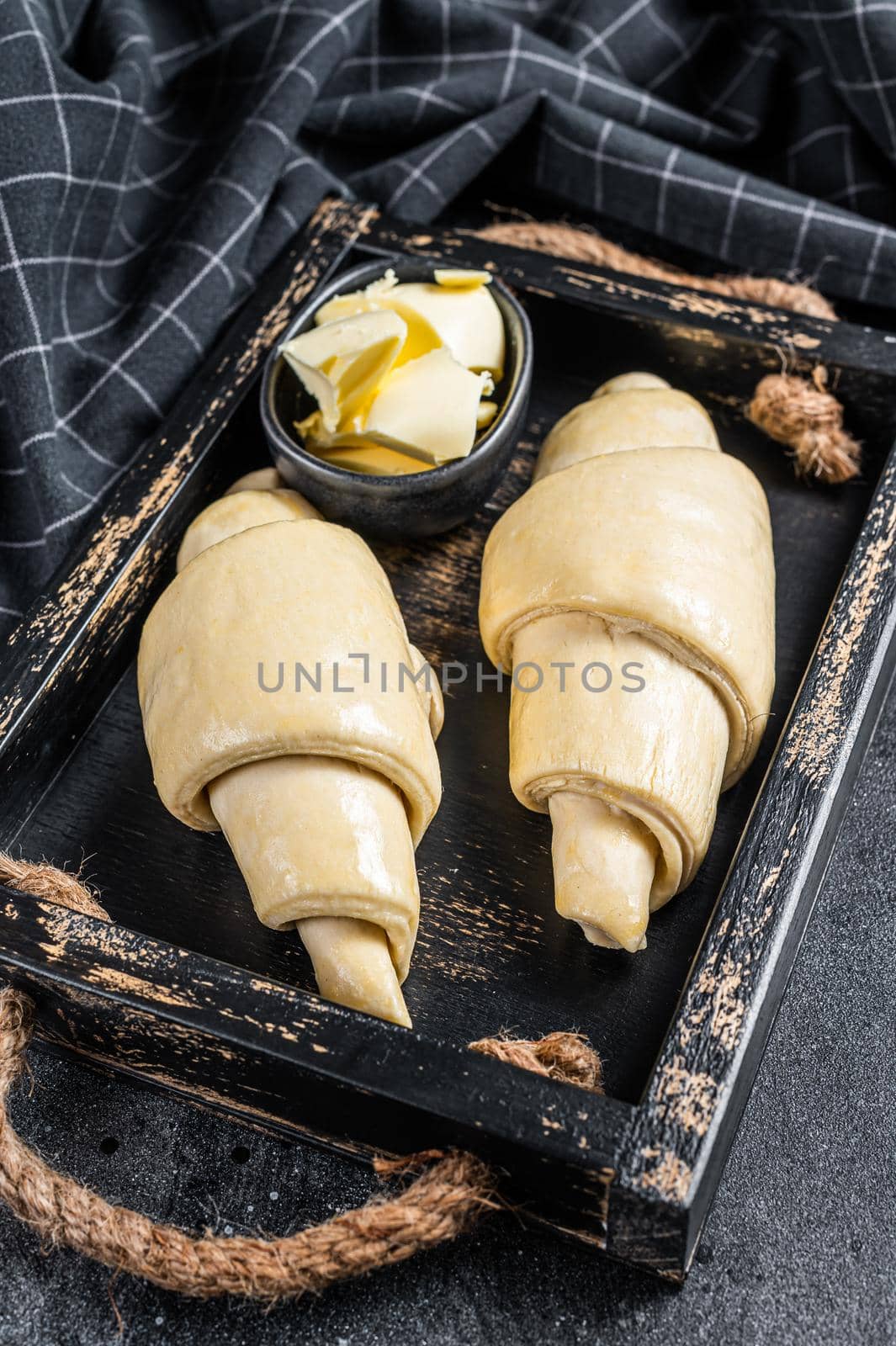 Raw fresh croissant in a wooden tray. Black background. Top view by Composter