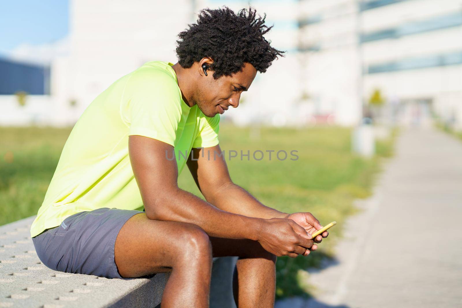 Black man with afro hair and earphones consulting his smartphone with some exercise app while resting from his workout.