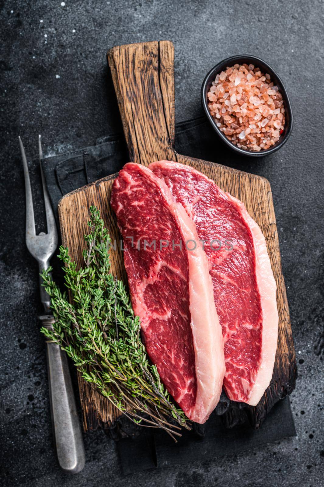 Uncooked Raw rump steak or top sirloin cap beef meat steaks on wooden board. Black background. Top view by Composter