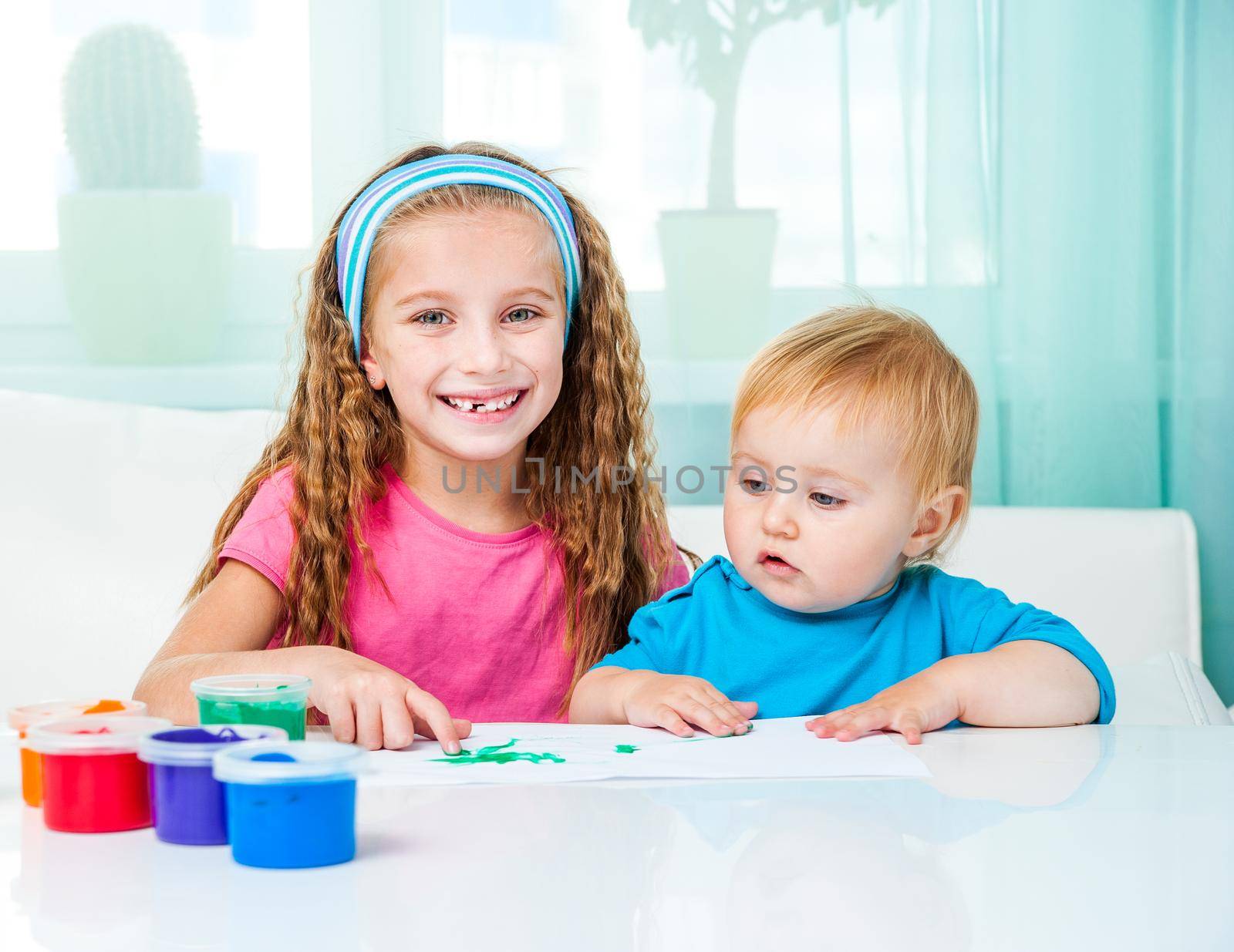 two smiling little sisters draw finger paints at home in bright living room