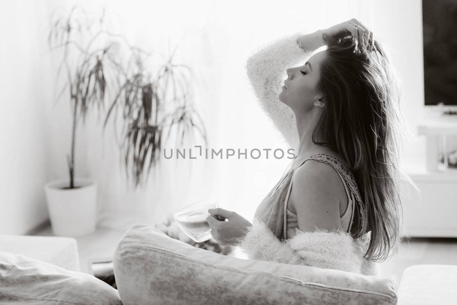 a relaxed girl at home drinks coffee and watches a movie.Domestic calm.The girl is sitting comfortably on the sofa and drinking coffee.black and white photo.