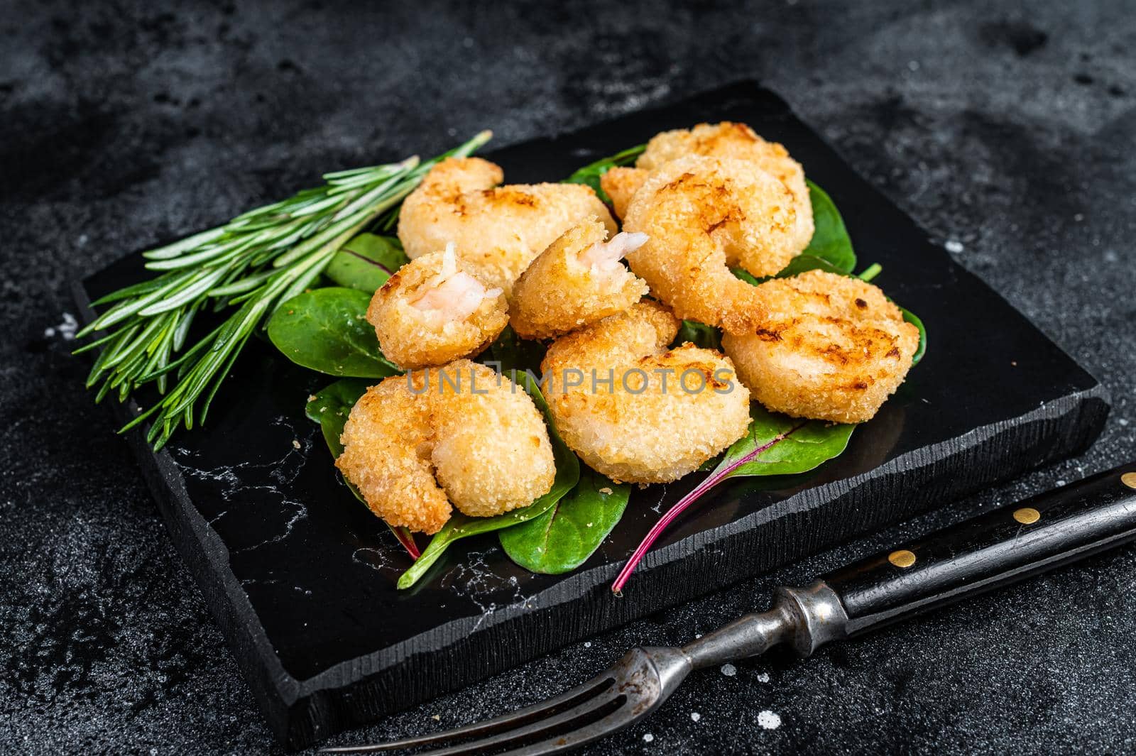 Roasted Crispy Shrimps Prawns on a marble board with green salad. Black background. Top view.