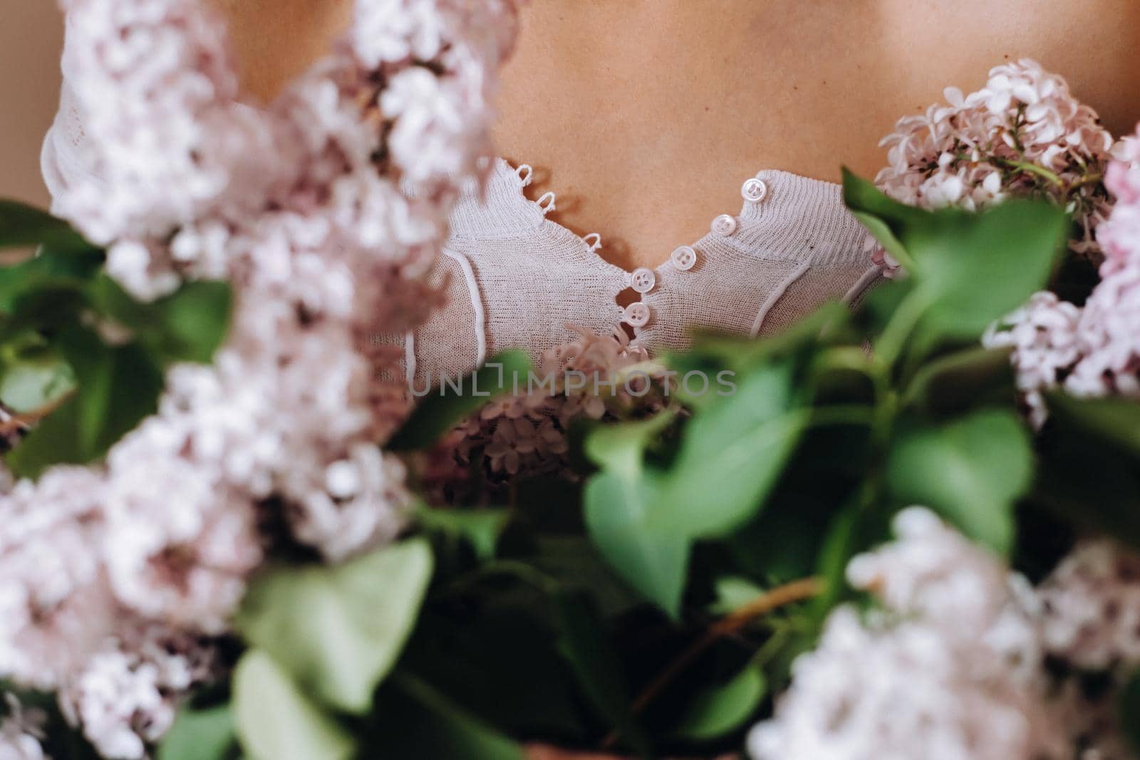 Beautiful girl with lilac flowers in her hands. A girl with lilac flowers in the spring at home. A girl with long hair and lilac in her hands.