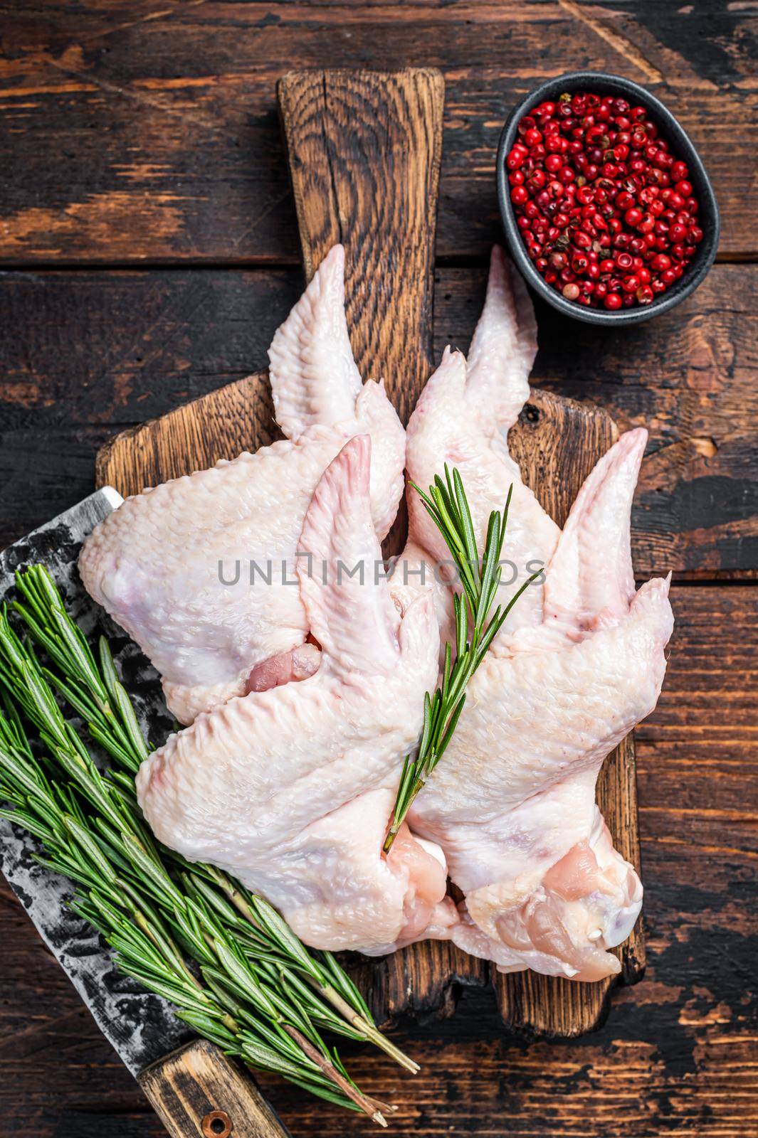 Uncooked Raw chicken wings Poultry meat on a butchery board with meat cleaver. Dark Wooden background. Top view by Composter