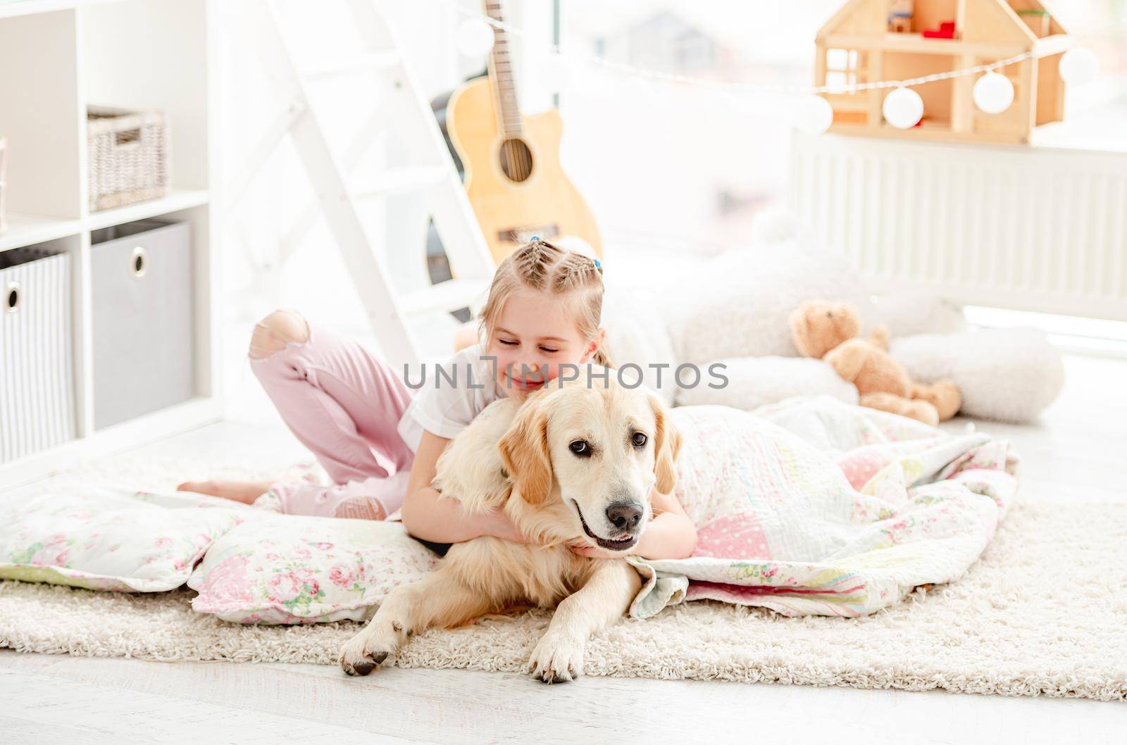 Cute little girl hugging adorable dog on blanket indoors