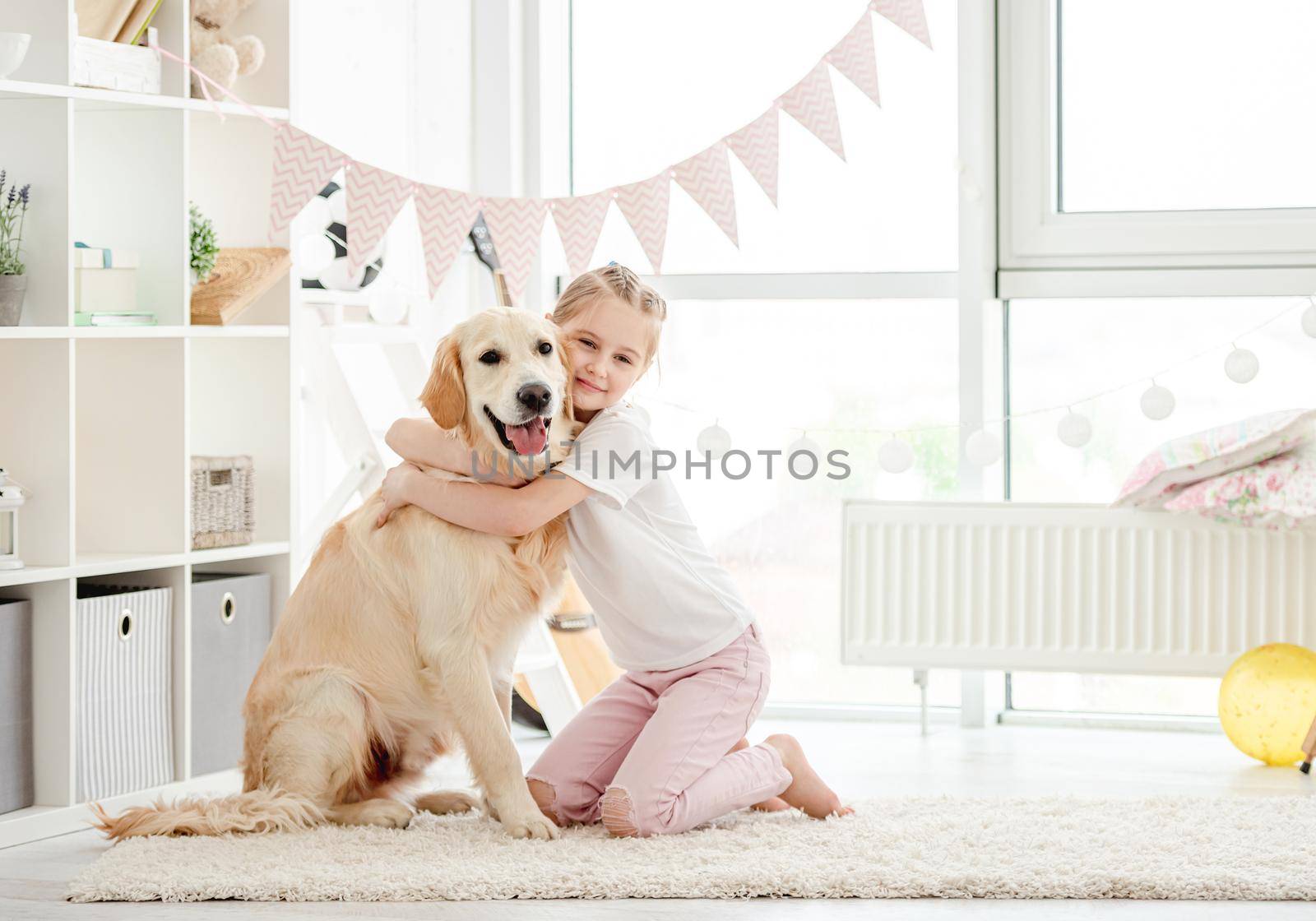 Pretty little girl embracing cute dog in light playroom