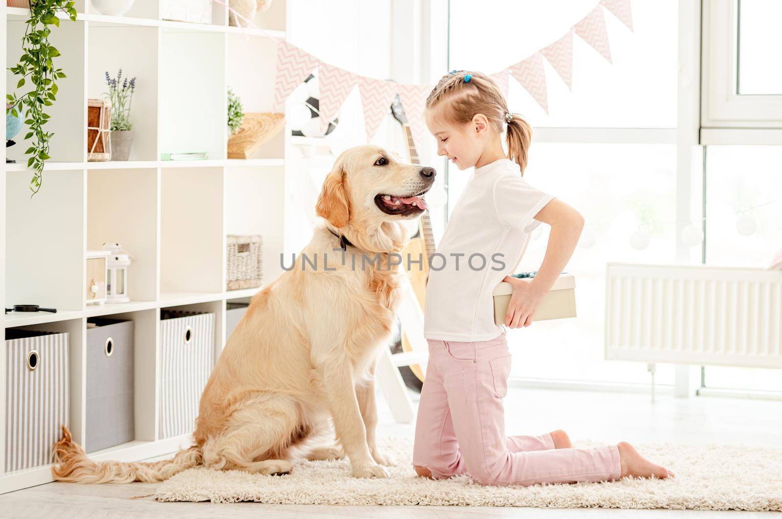 Beautiful little girl presenting gift to cute dog indoors