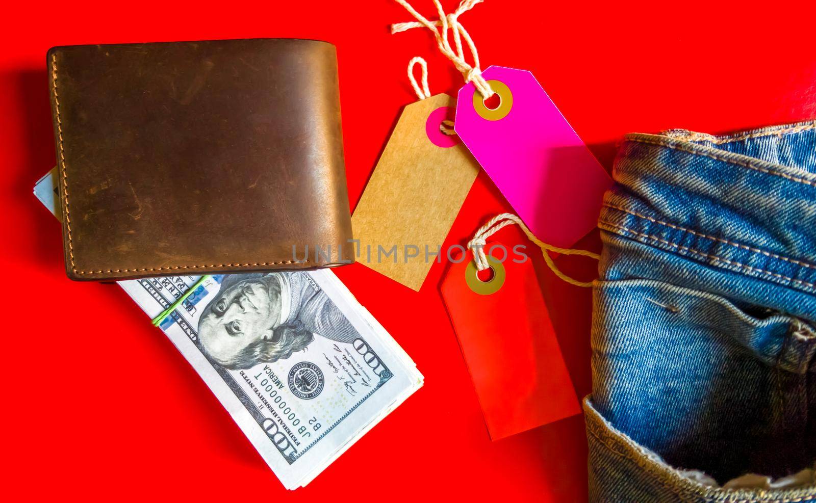 Many hundreds of dollars banknotes in a leather wallet with colored cardboard tags, price tags on a red background. Flat lay. Background, holiday concept. Black Friday - International Day of Shopping, Promotions, Discounts, Sales. Sales season is the fourth Thursday of November.