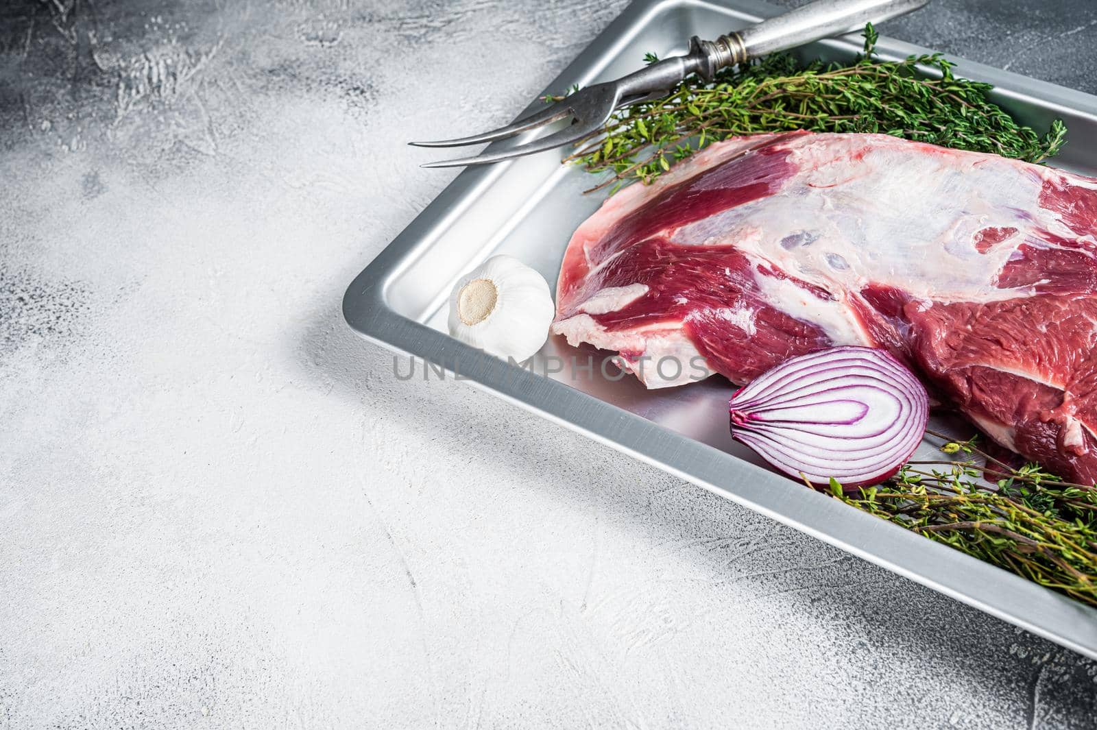 Raw lamb mutton shoulder meat in a baking dish with thyme and garlic. White background. Top view. Copy space by Composter