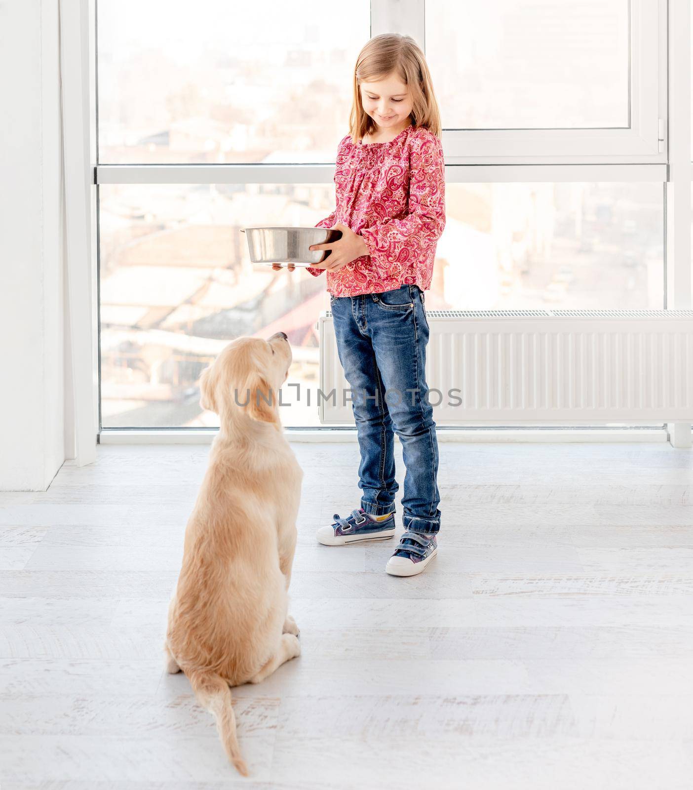 Lovely little girl giving food to her beautiful dog indoors