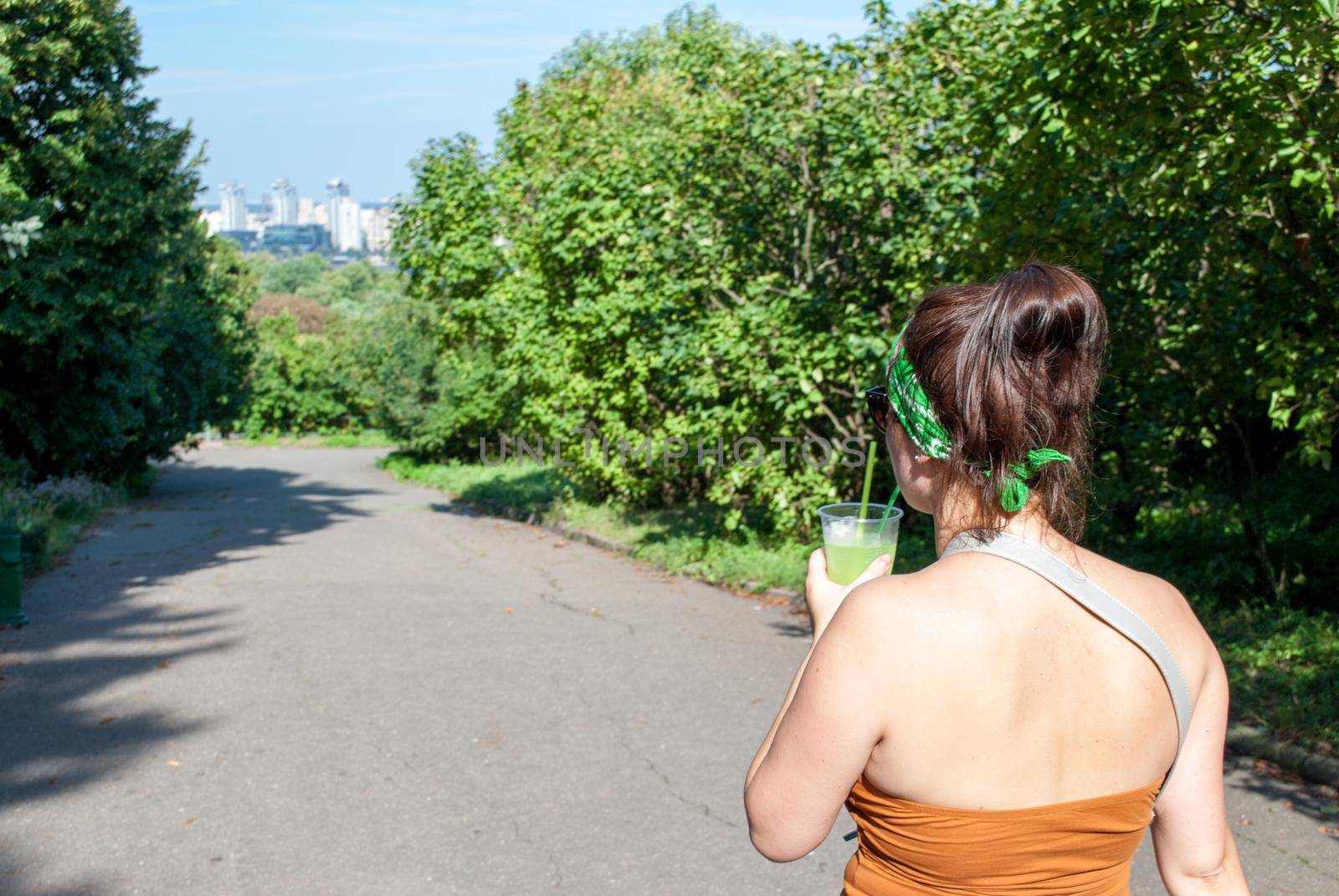 Young beautiful girl drinking a green drink from a plastic cup takeaway food. Summer cold drinks.