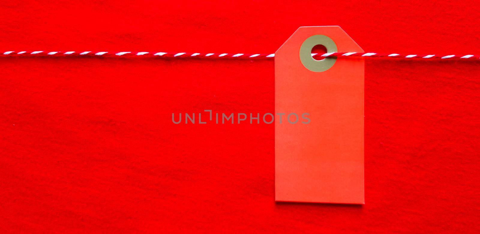 Red tag tag hanging on a red rope on a red background. Copy space, place for text, flat lay