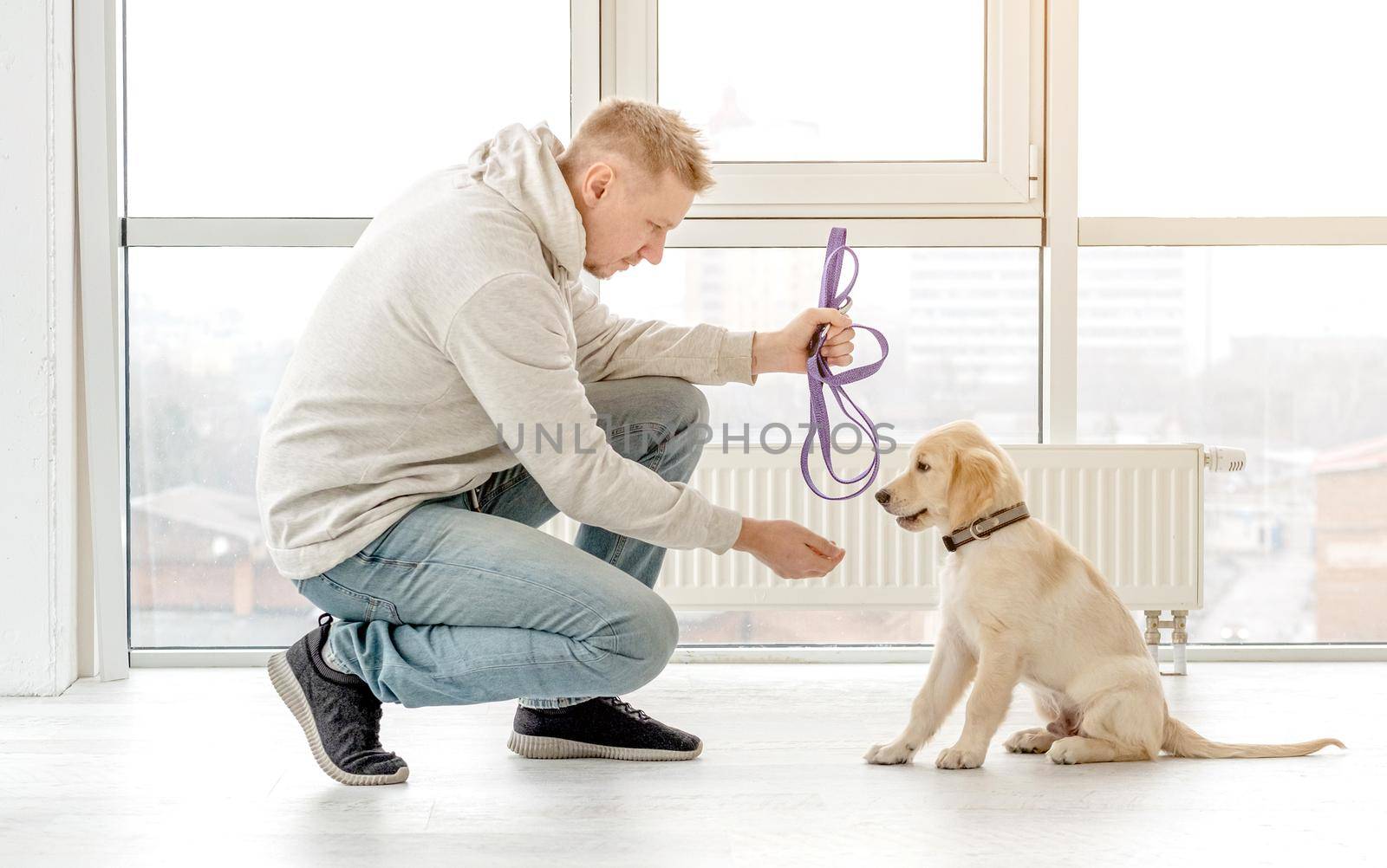 Handsome man holding leash near retriever puppy indoors