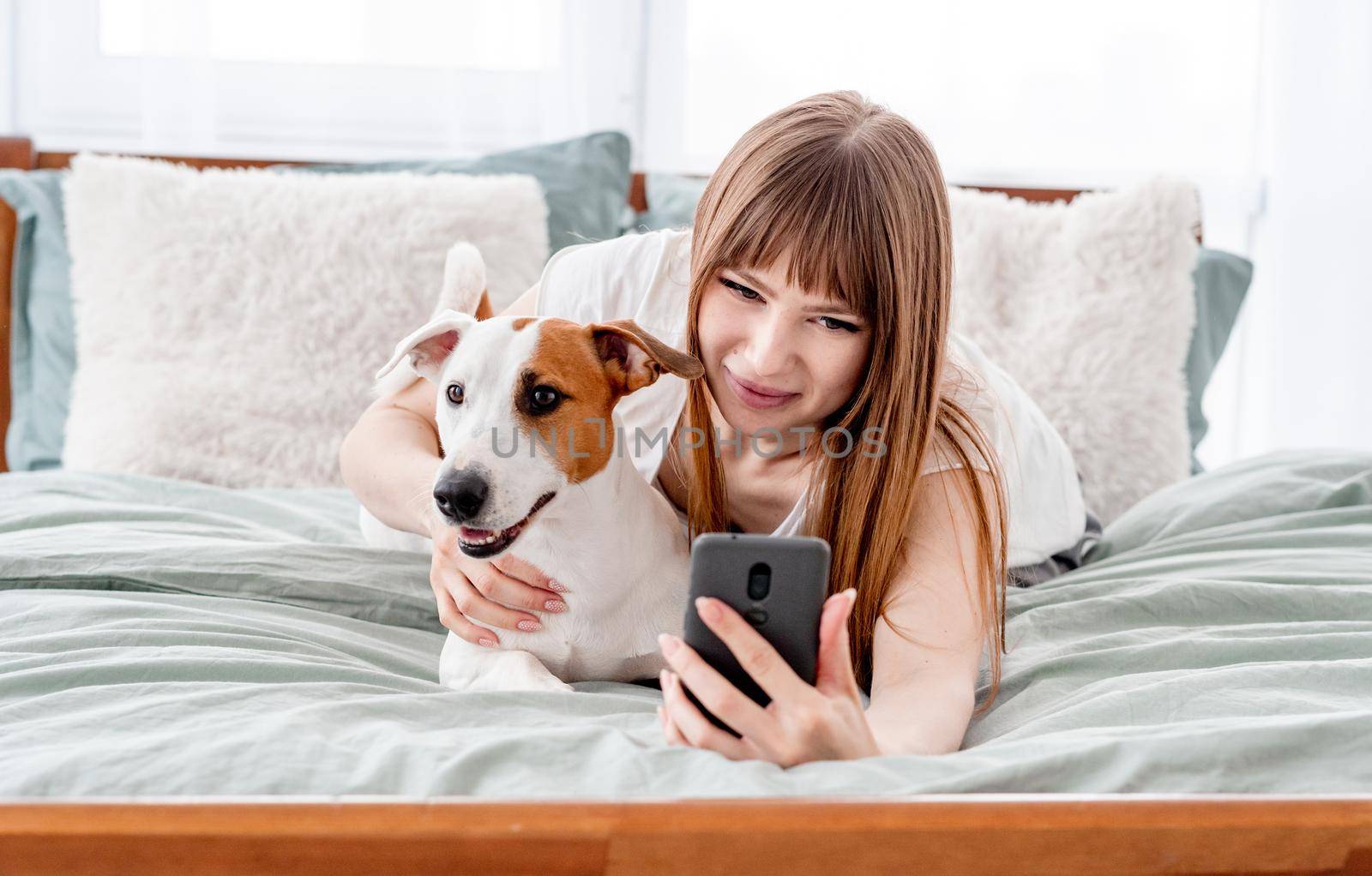 Girl with dog and smartphone in the bed by tan4ikk1