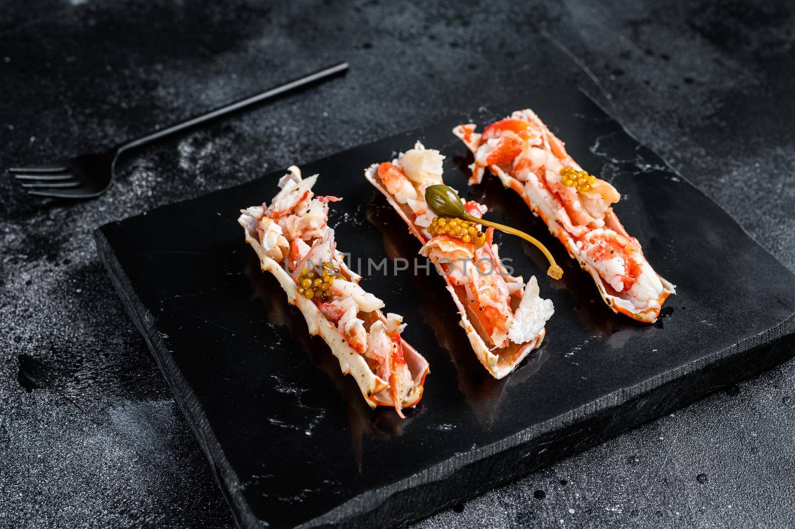 Crab leg meat in a sheel with herbs. Black background. Top view by Composter