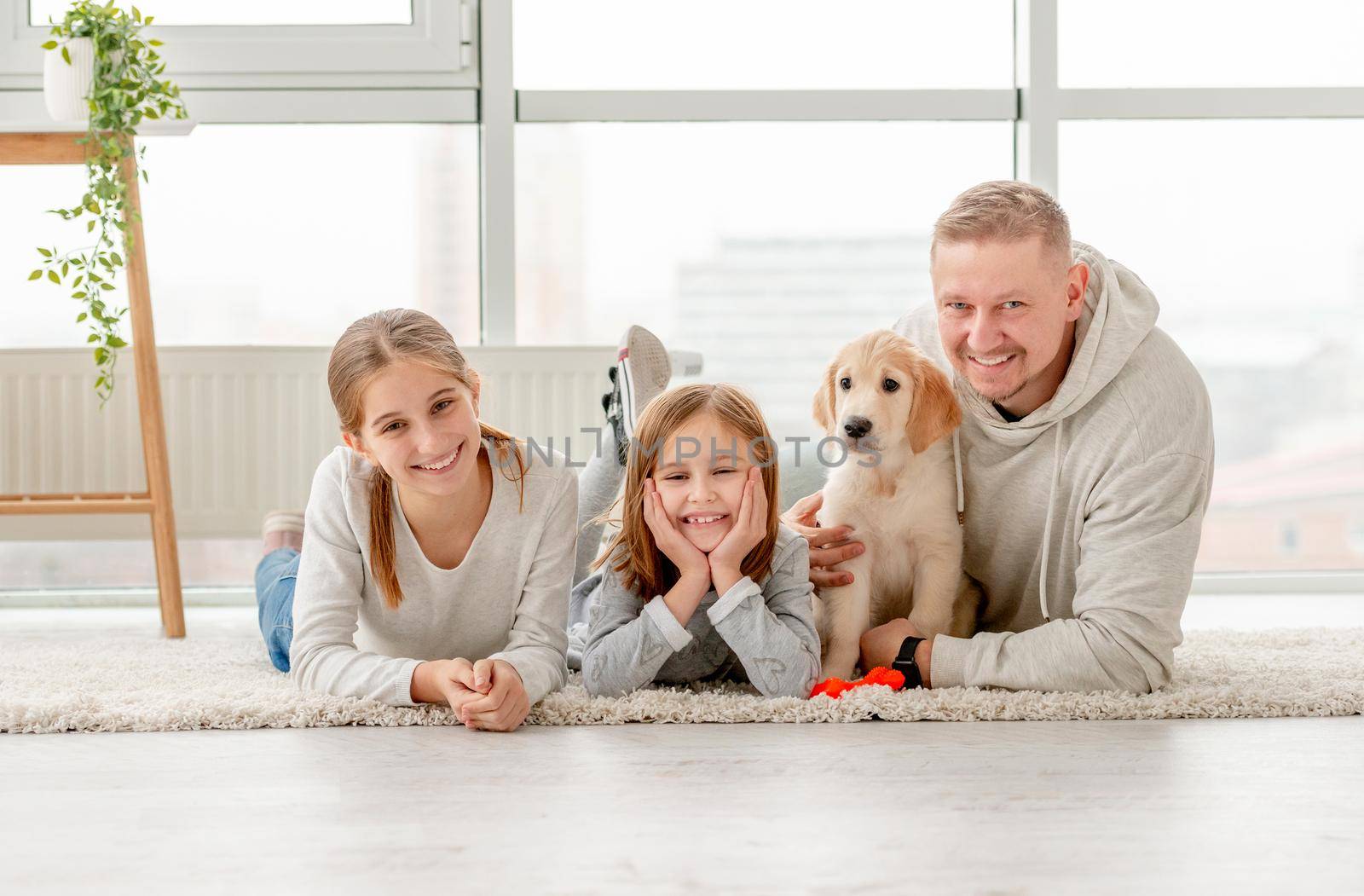 Smiling father with cute daughters and lovely puppy lying indoors