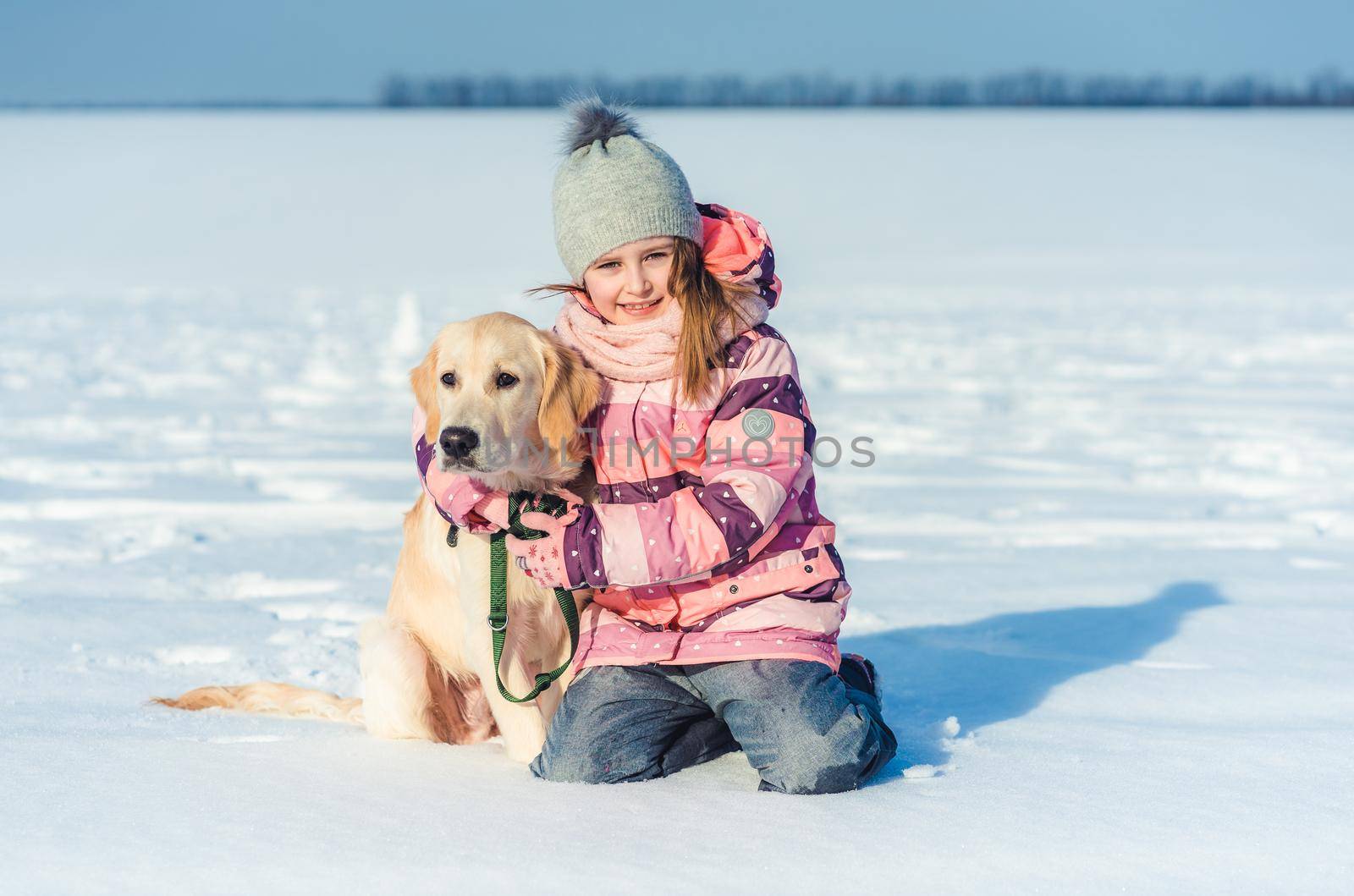 Charming little girl sitting on snow next to loyal dog
