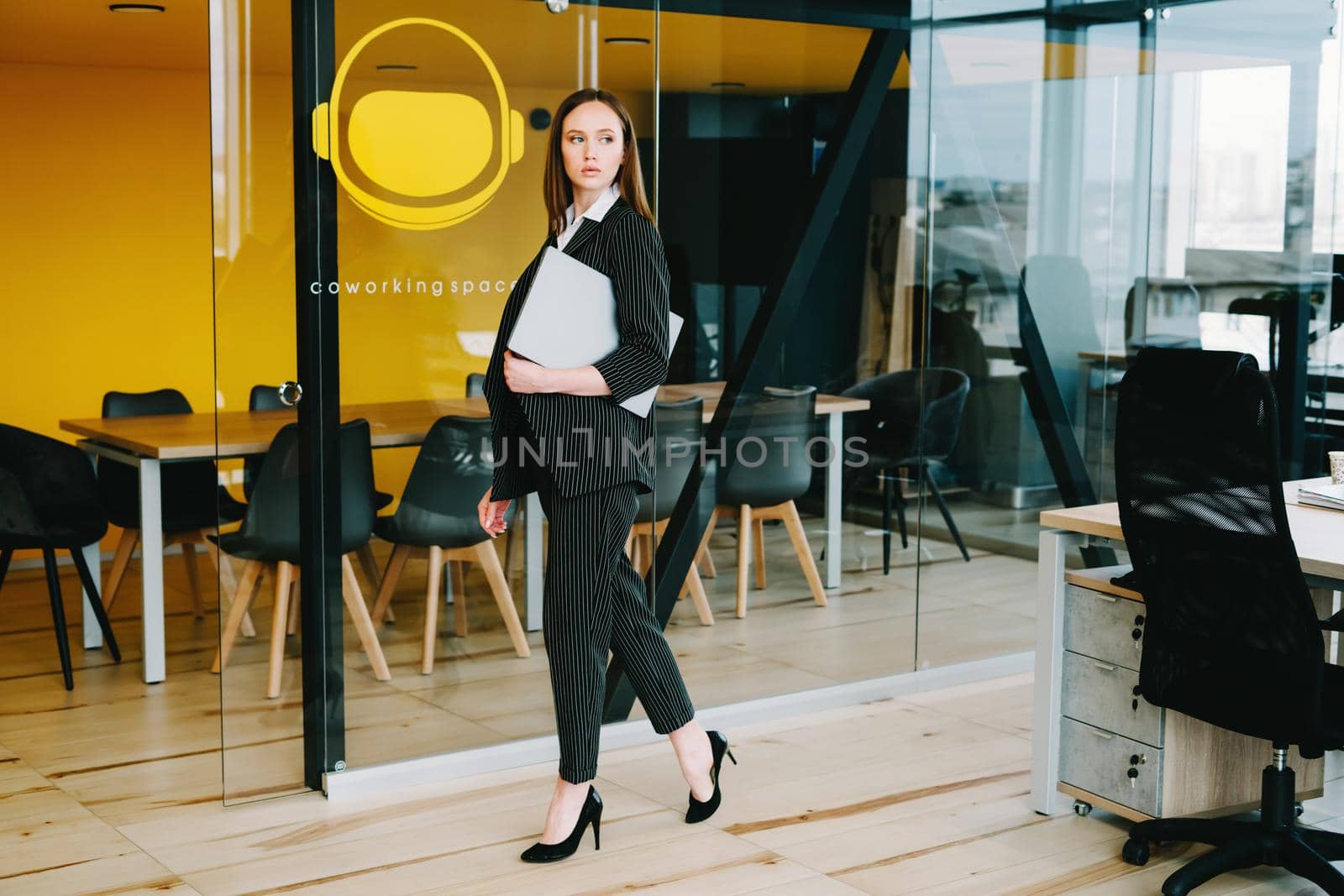 Business lady in a stylish office. A girl in the office with a laptop. Freelancer. Manager. Spacious office with glass partitions and doors, yellow and black walls.