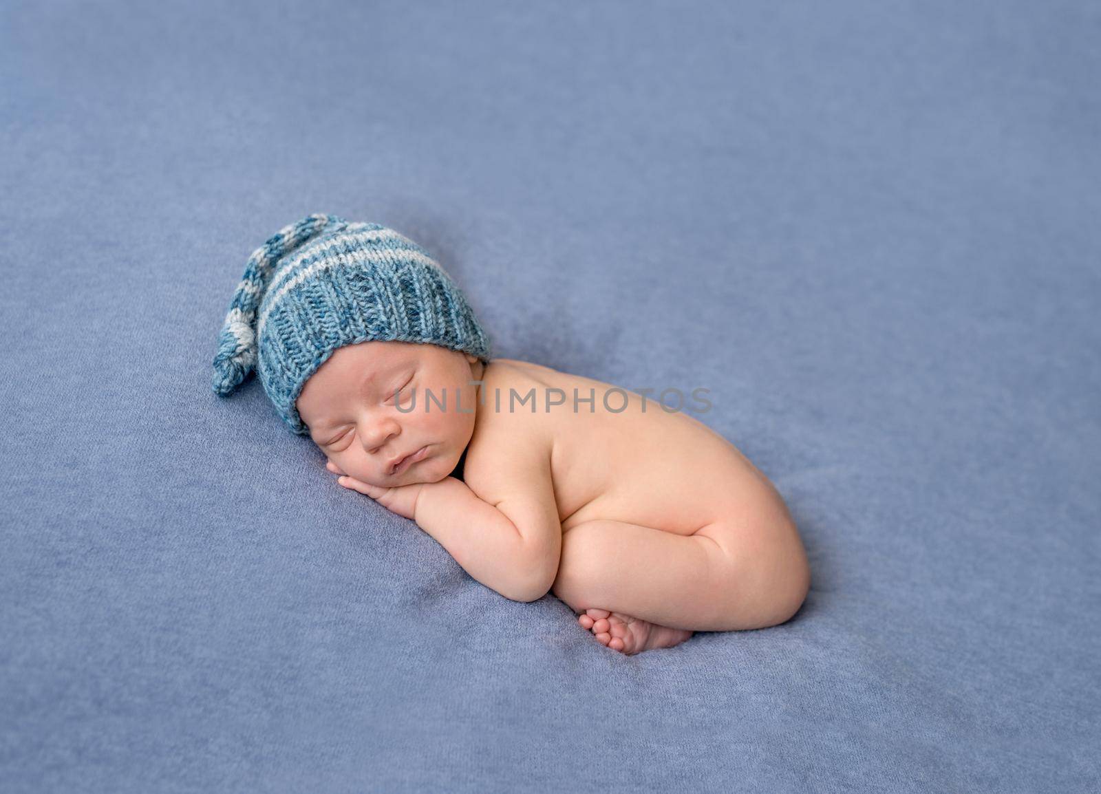 lovely naked newborn in knitted hat sleeping on gray blanket