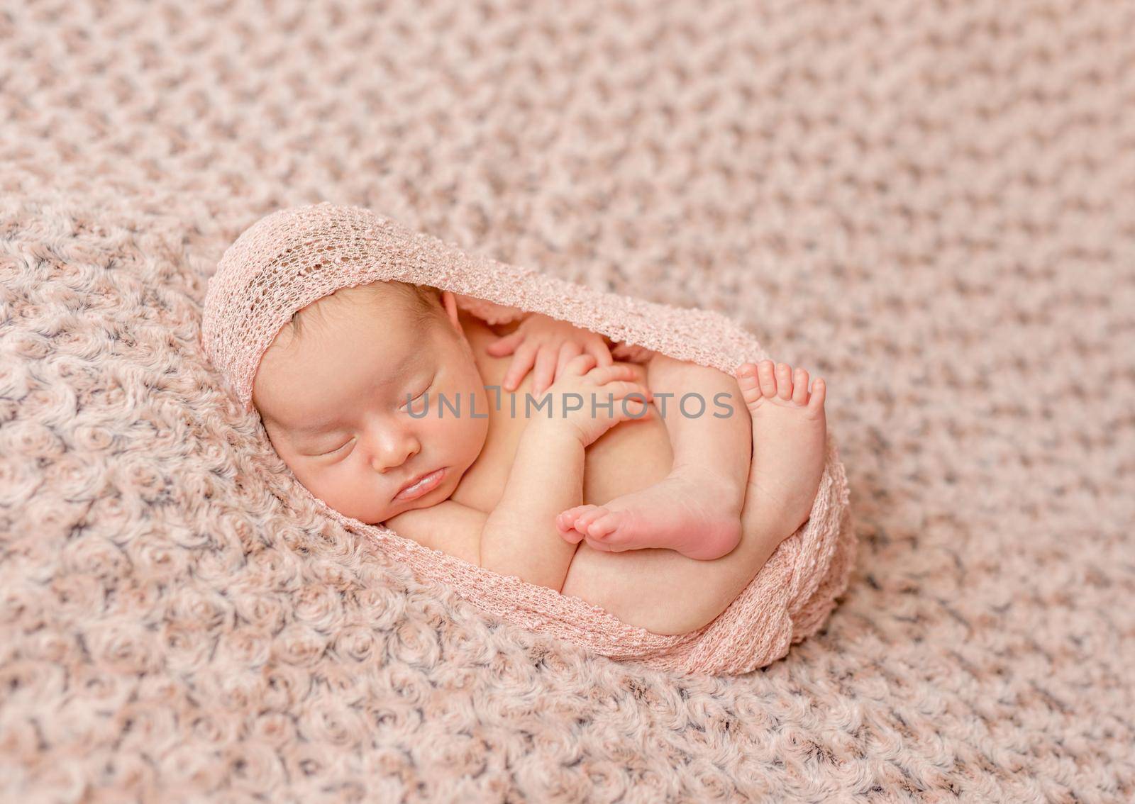 lovely newborn curled up asleep, wrapped in pink diaper on knitted blanket