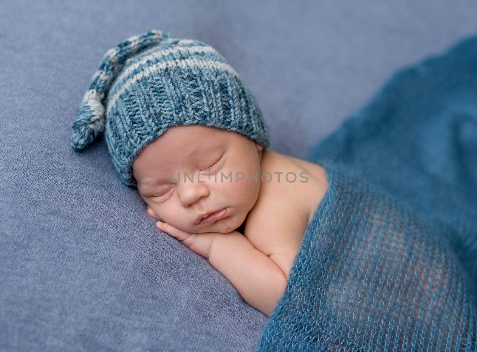 portrait of sweet sleeping newborn baby in hat covered with blanket