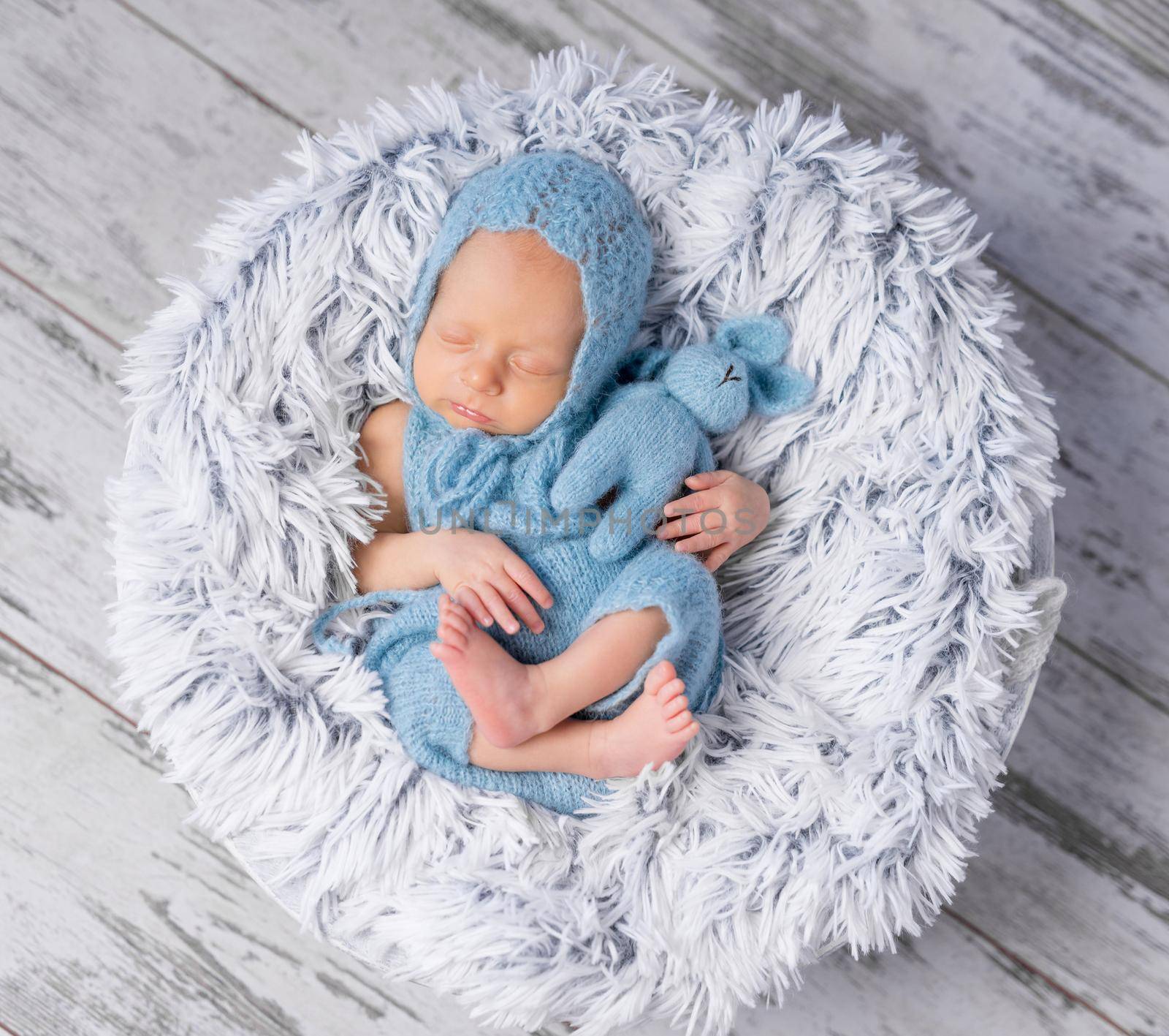 lovely infant in hat and jumpsuit sleeping on round little bed, top view