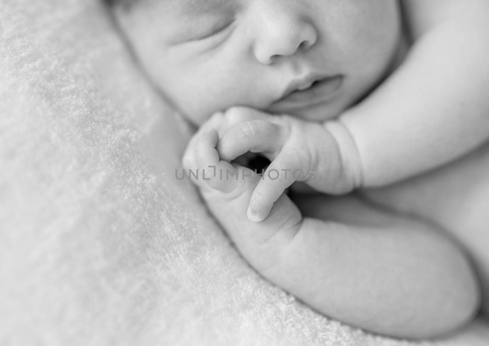 lovely sleepy face and hands with crossed fingers of a newborn baby, black and white photo, close up