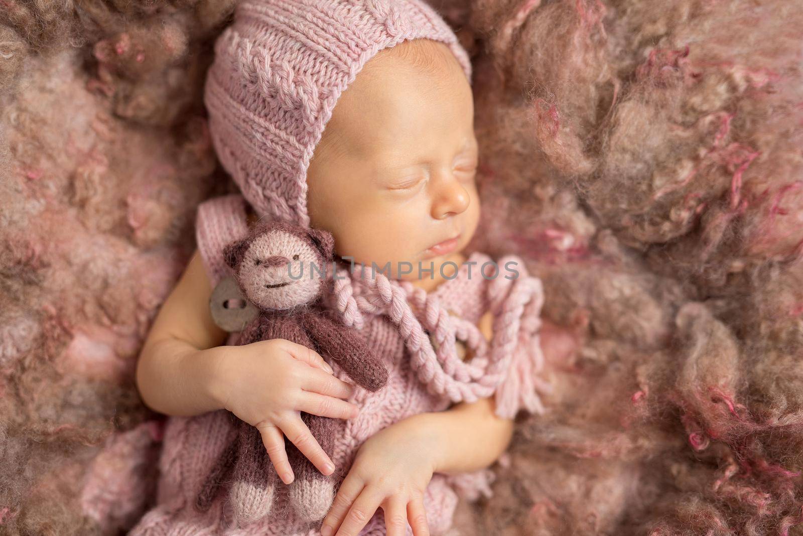 cute newborn baby on fluffy blanket in pink knitted hat and suit, with toy in hand