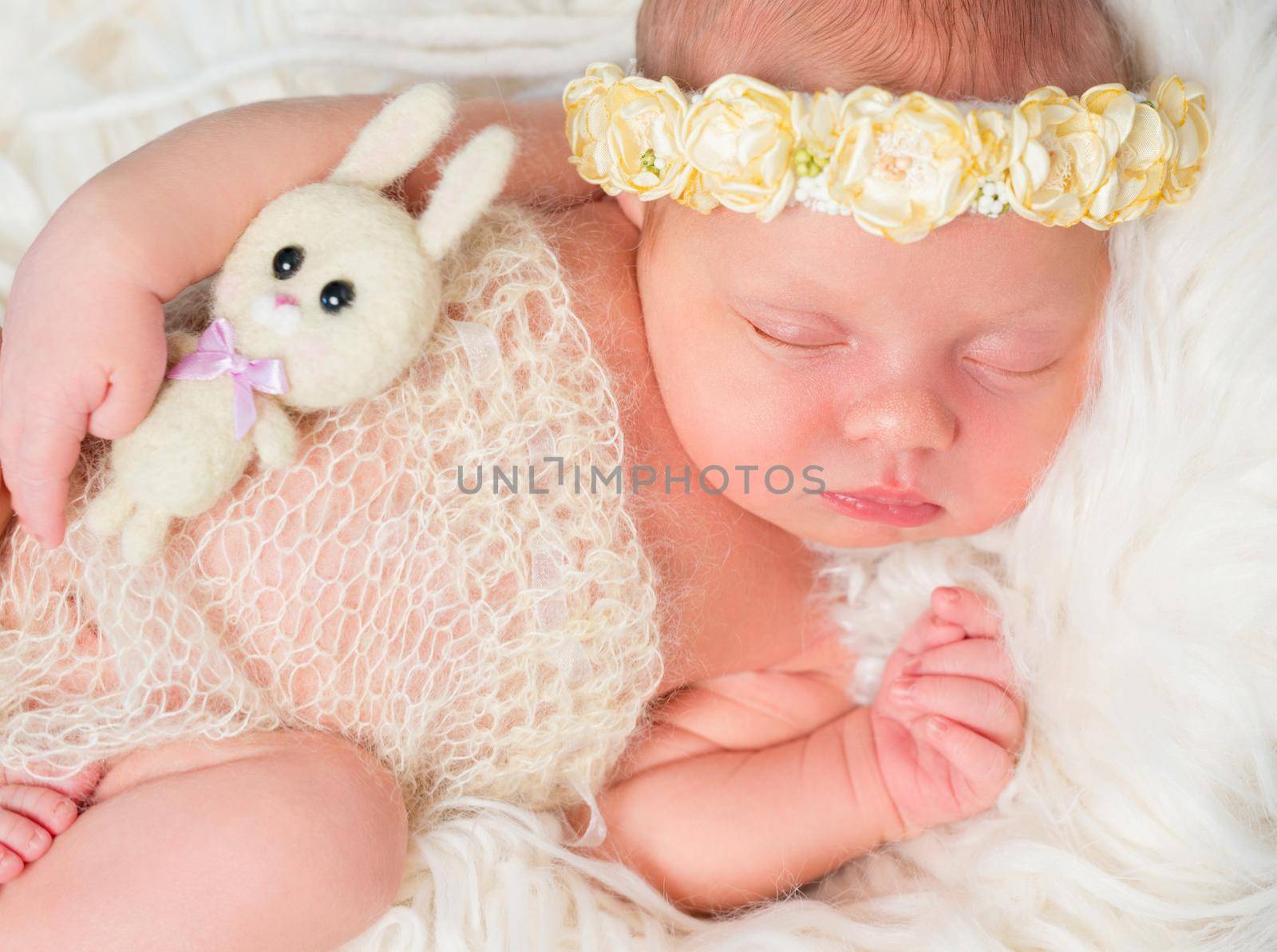 beautiful sleeping newborn girl with little toy and headband with flowers