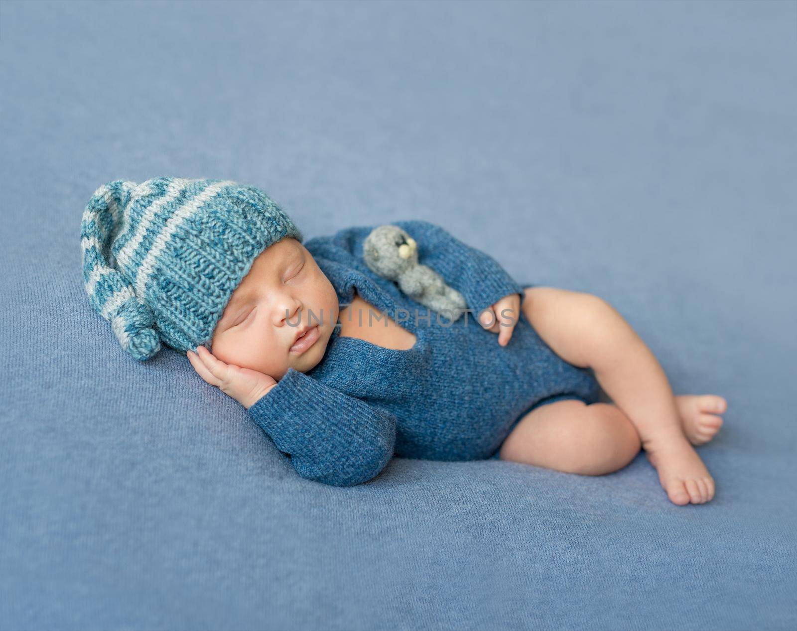 sleeping newborn baby in blue knitted jumpsuit and hat with crossed legs